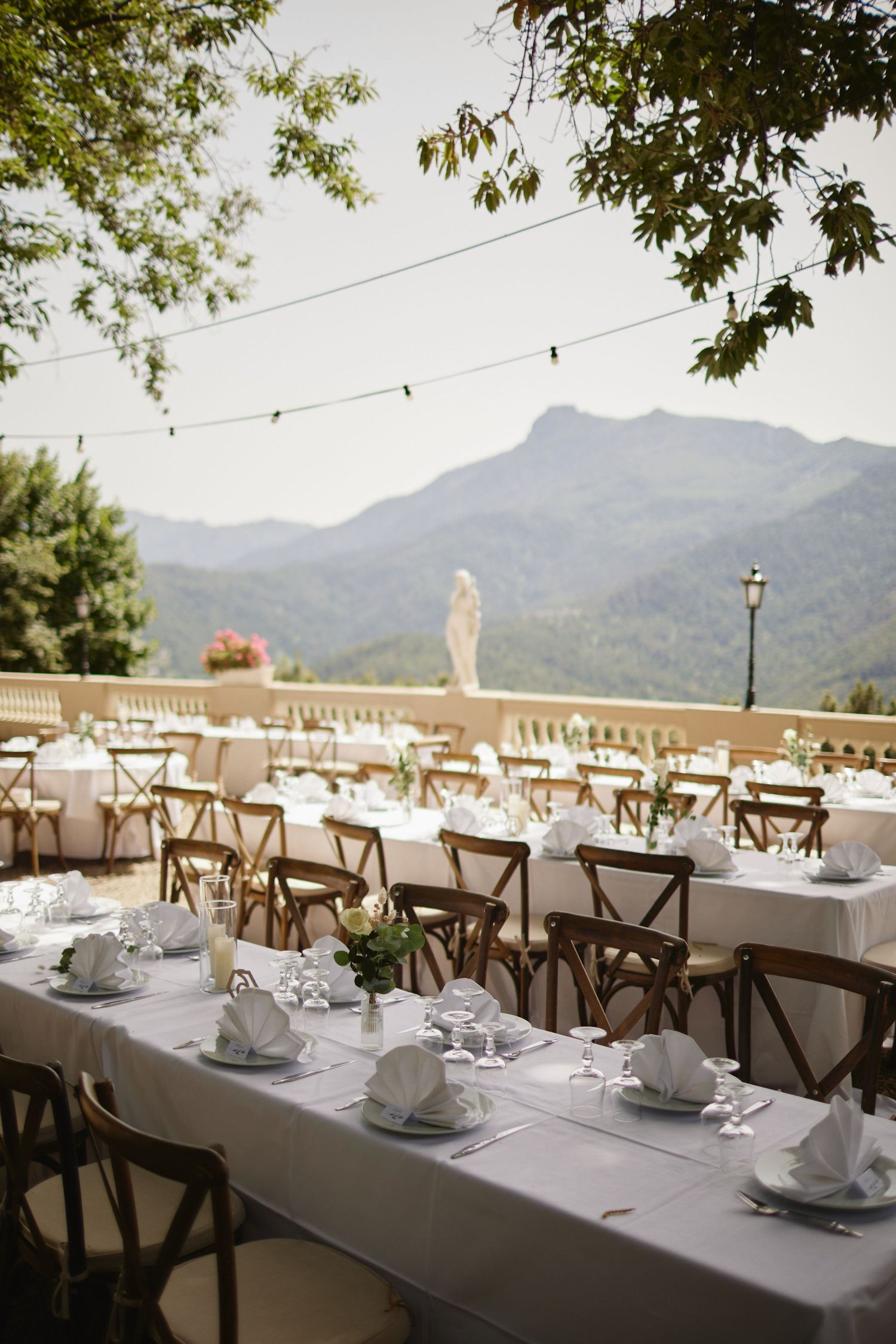 Elegant outdoor wedding reception tables set with white linens and napkins on a terrace with mountain views.