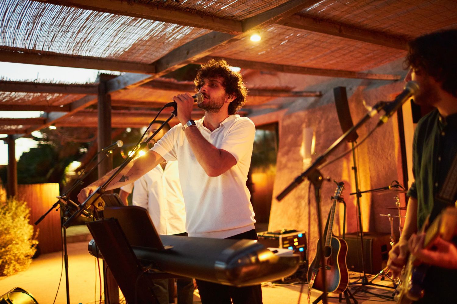 Musician performs at outdoor wedding reception, singing into microphone at keyboard on stage.
