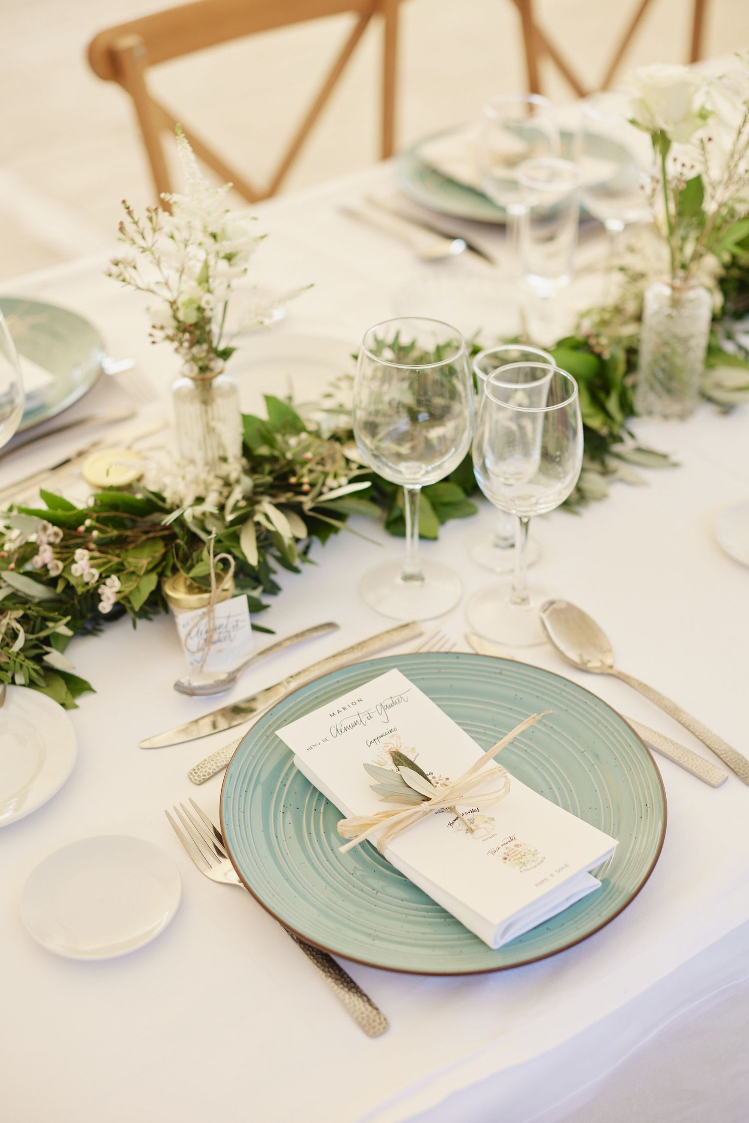 Elegant wedding reception table with sage green plates, gold cutlery, and white floral garland.