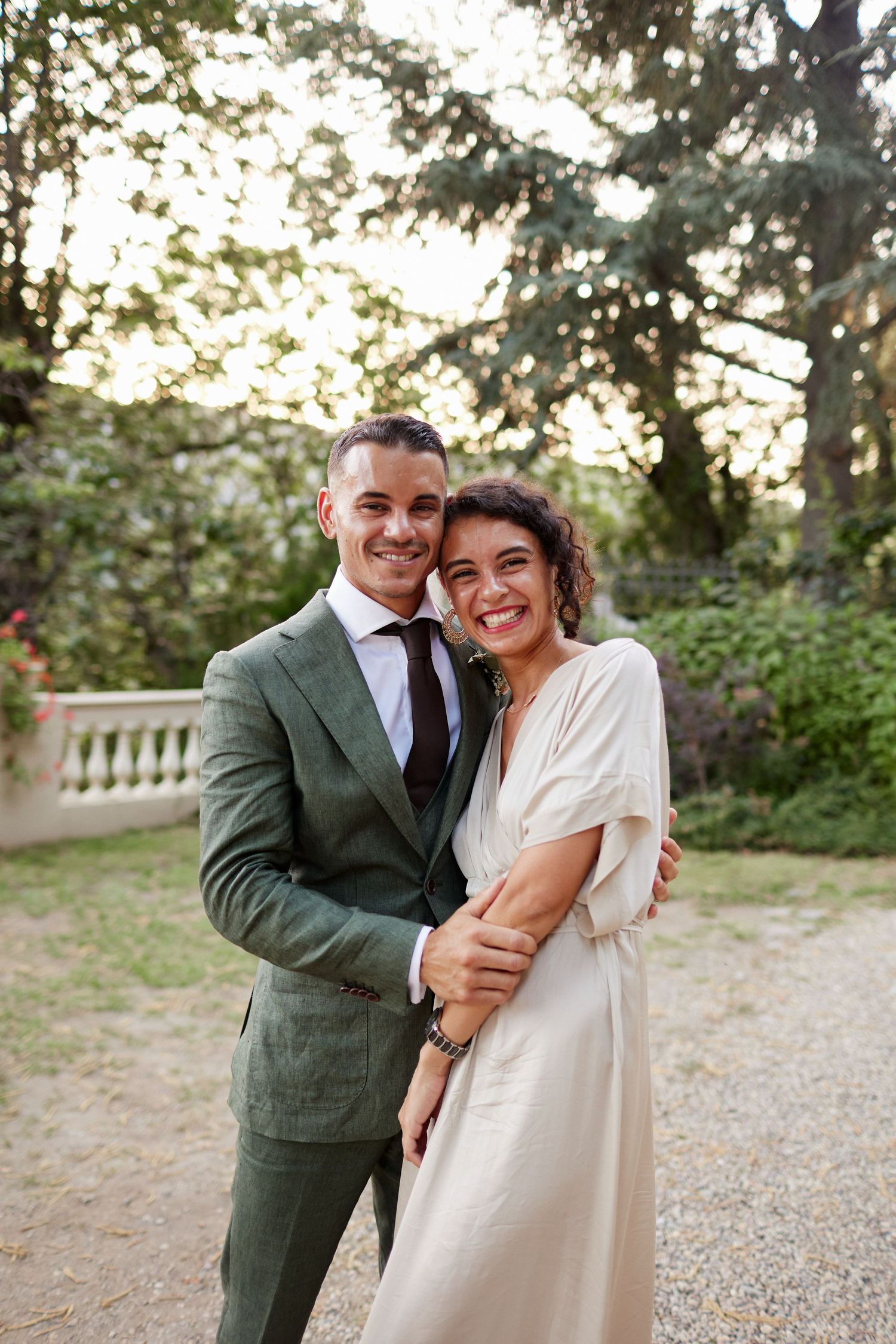 Smiling bride and groom embrace warmly in a lush garden at their wedding.