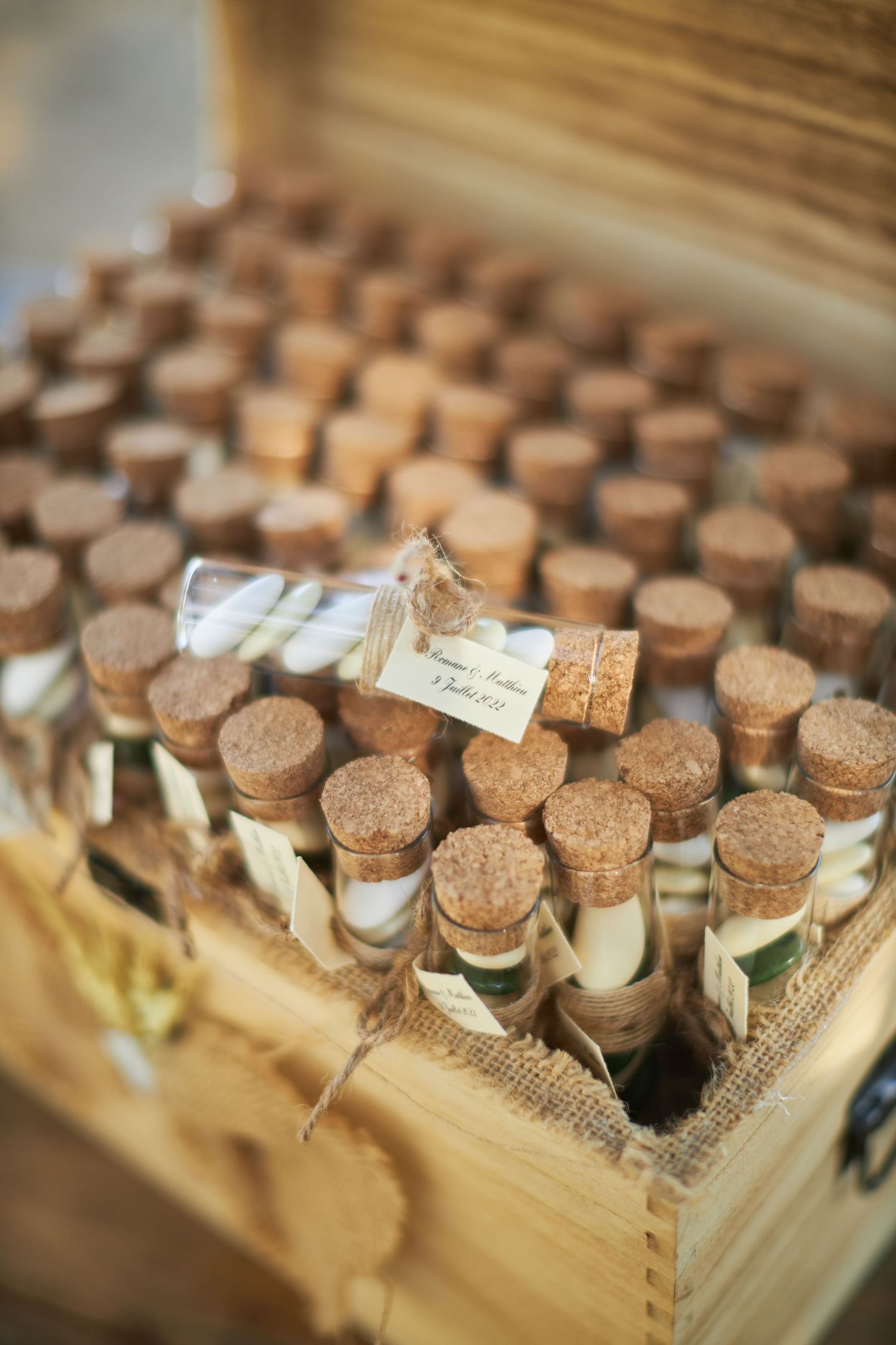 Cork-stoppered glass test tube wedding favors arranged in a rustic wooden box with burlap lining.