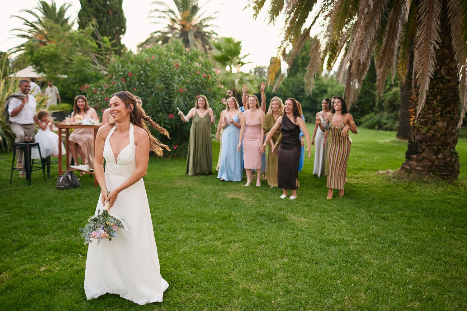 Bride preparing to toss bouquet to excited group of female guests at outdoor garden wedding.