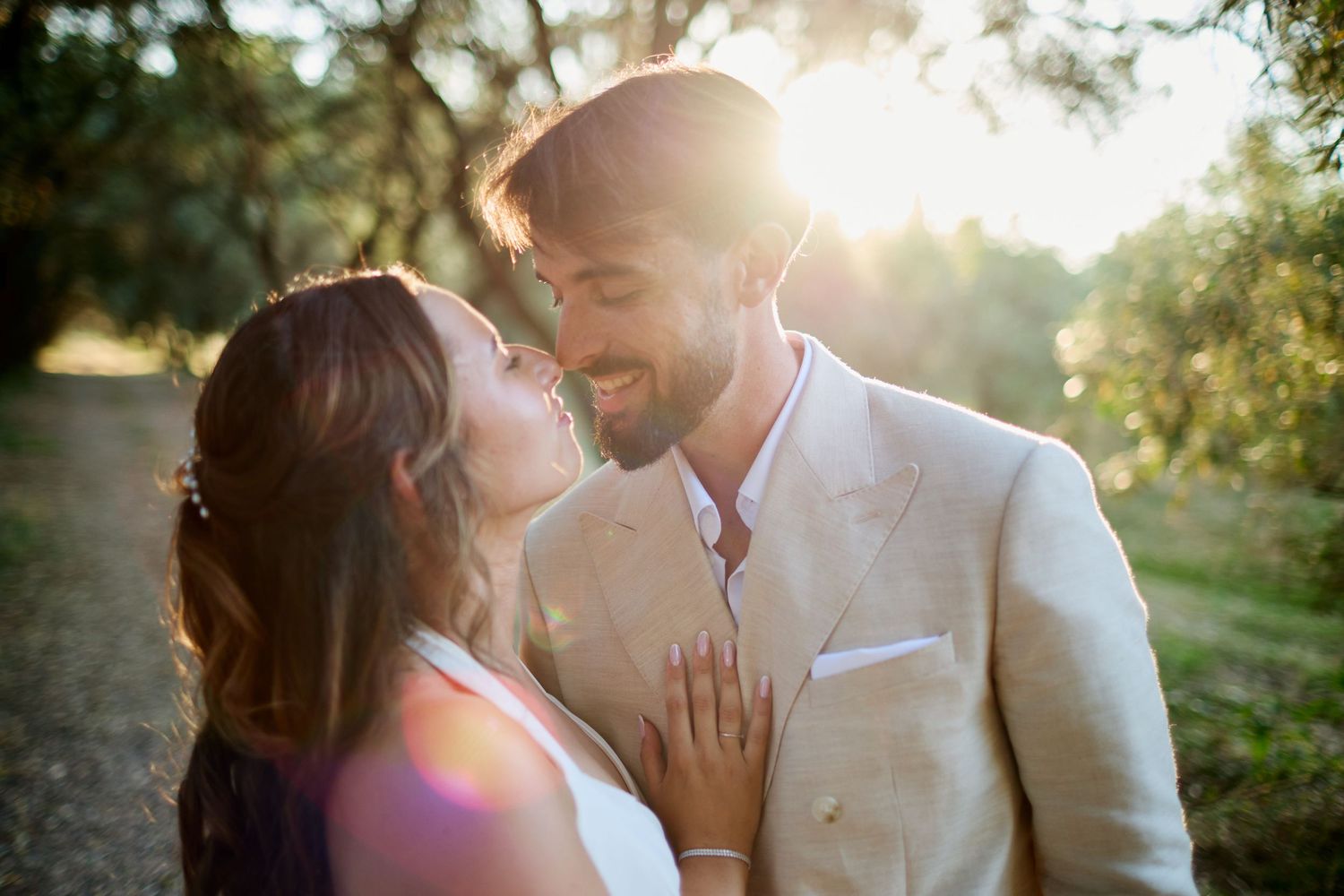 Bride and groom sharing a joyful close moment in warm golden sunlight surrounded by lush green trees.