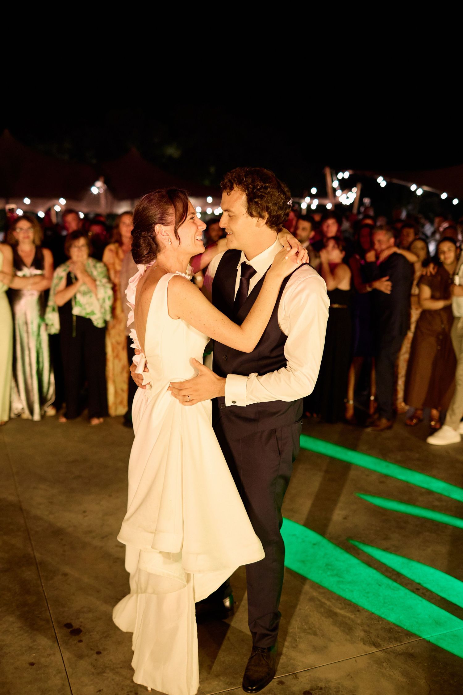 Bride and groom share romantic first dance at night with green lit dance floor.