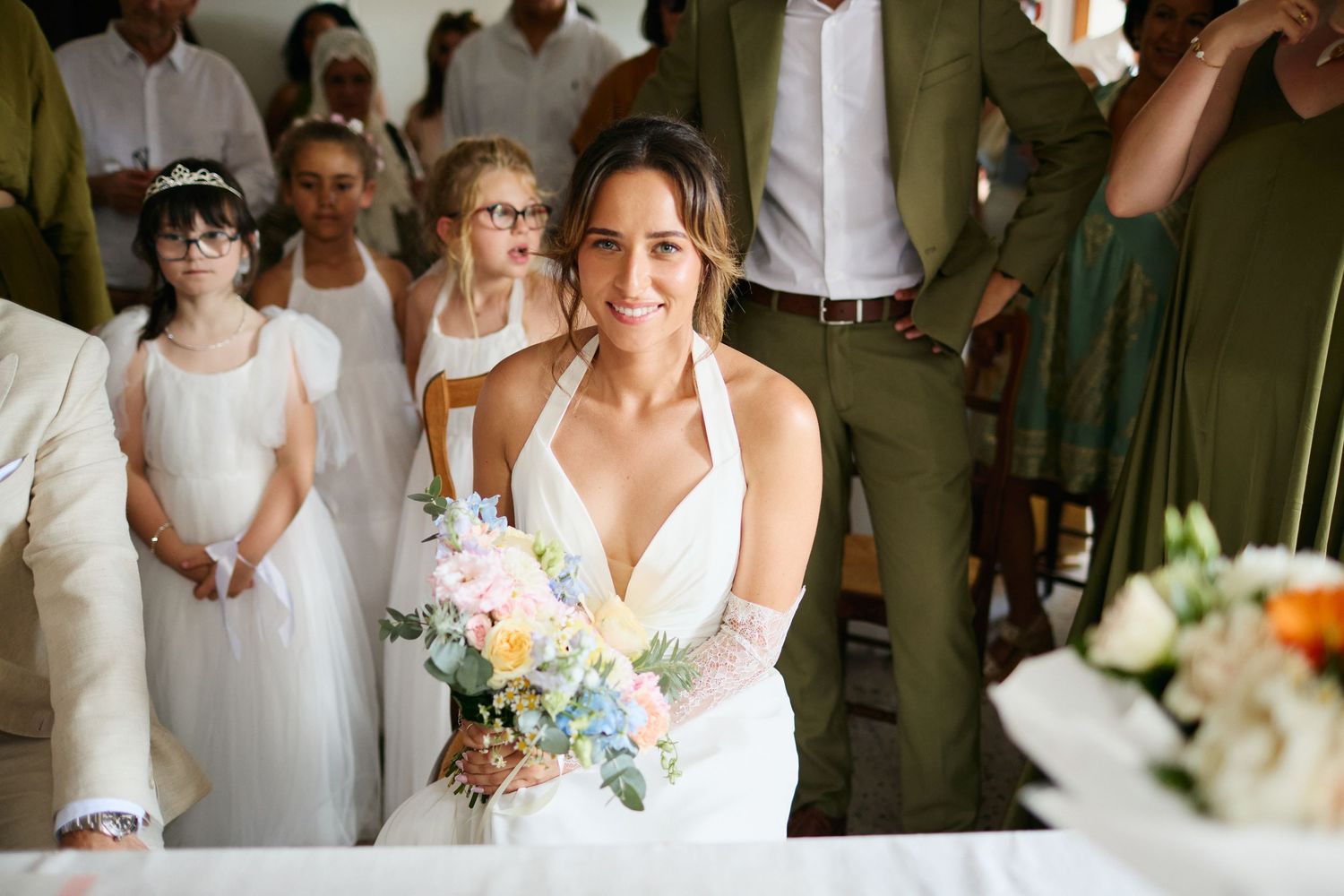 Radiant bride holding pastel bouquet smiles at wedding ceremony altar indoors.