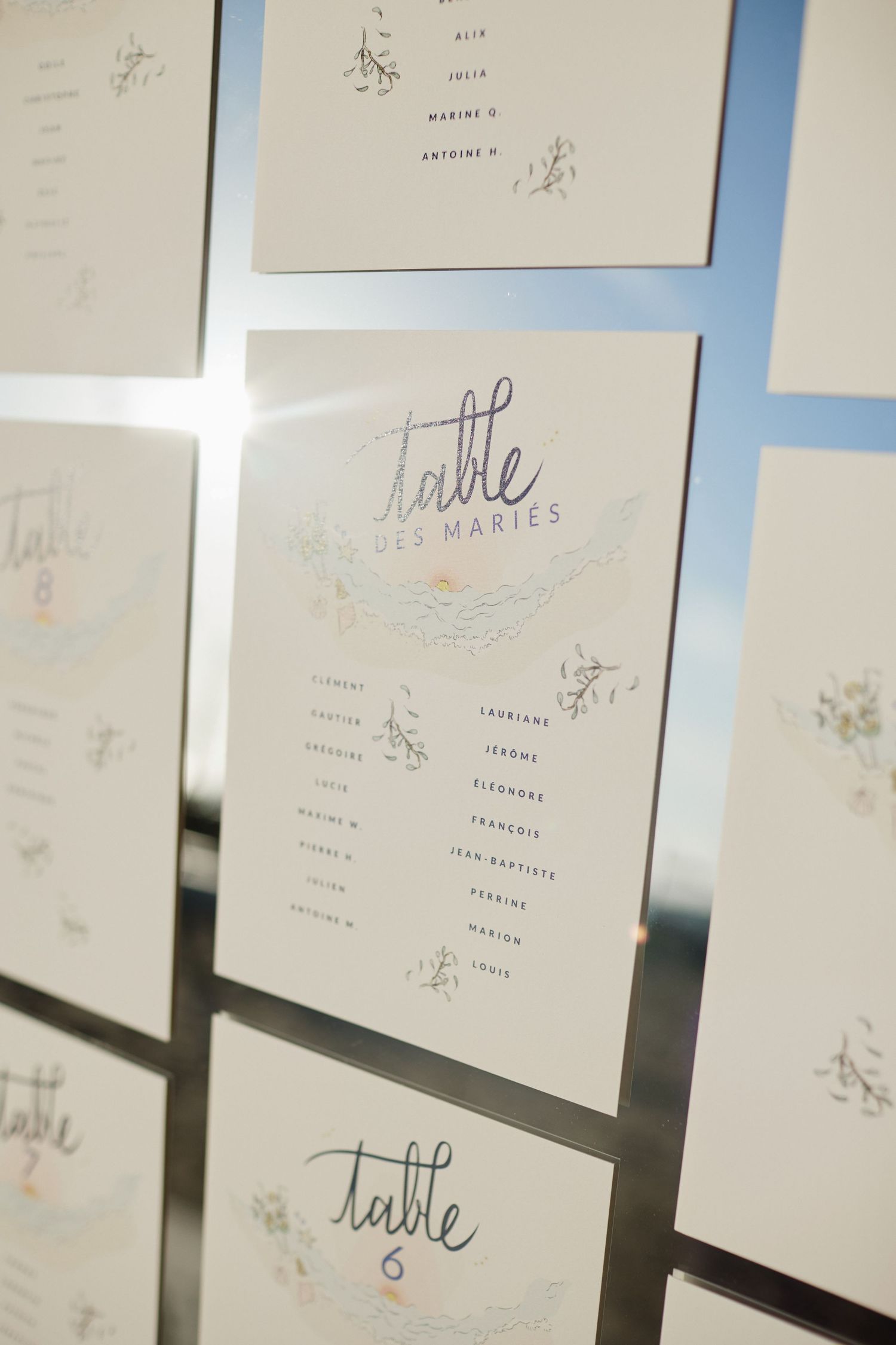 Elegant wedding seating chart cards displayed on a mirrored surface with calligraphy table assignments.