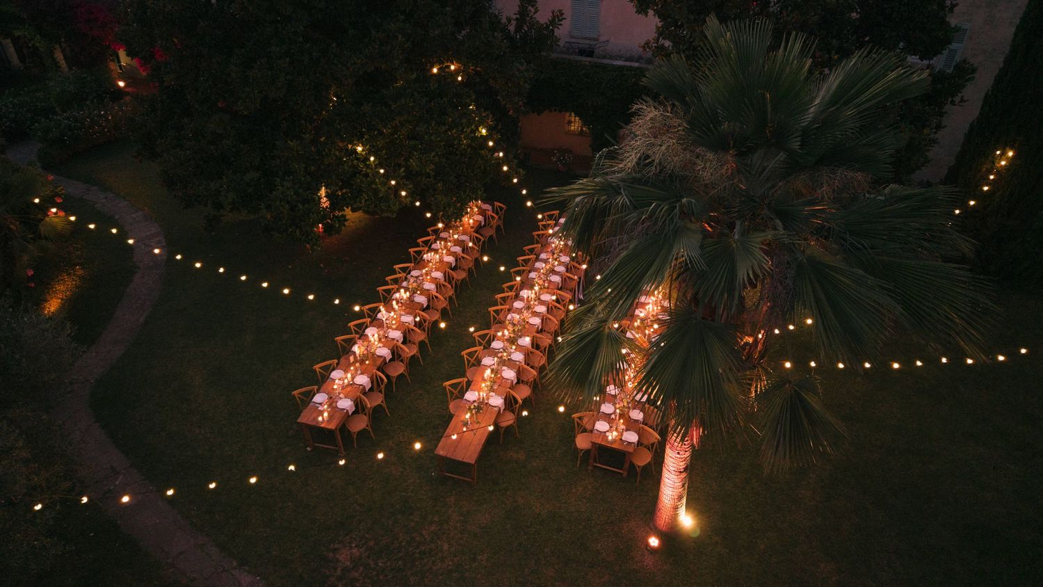 Aerial view of elegant candlelit wedding dinner tables under string lights at night.