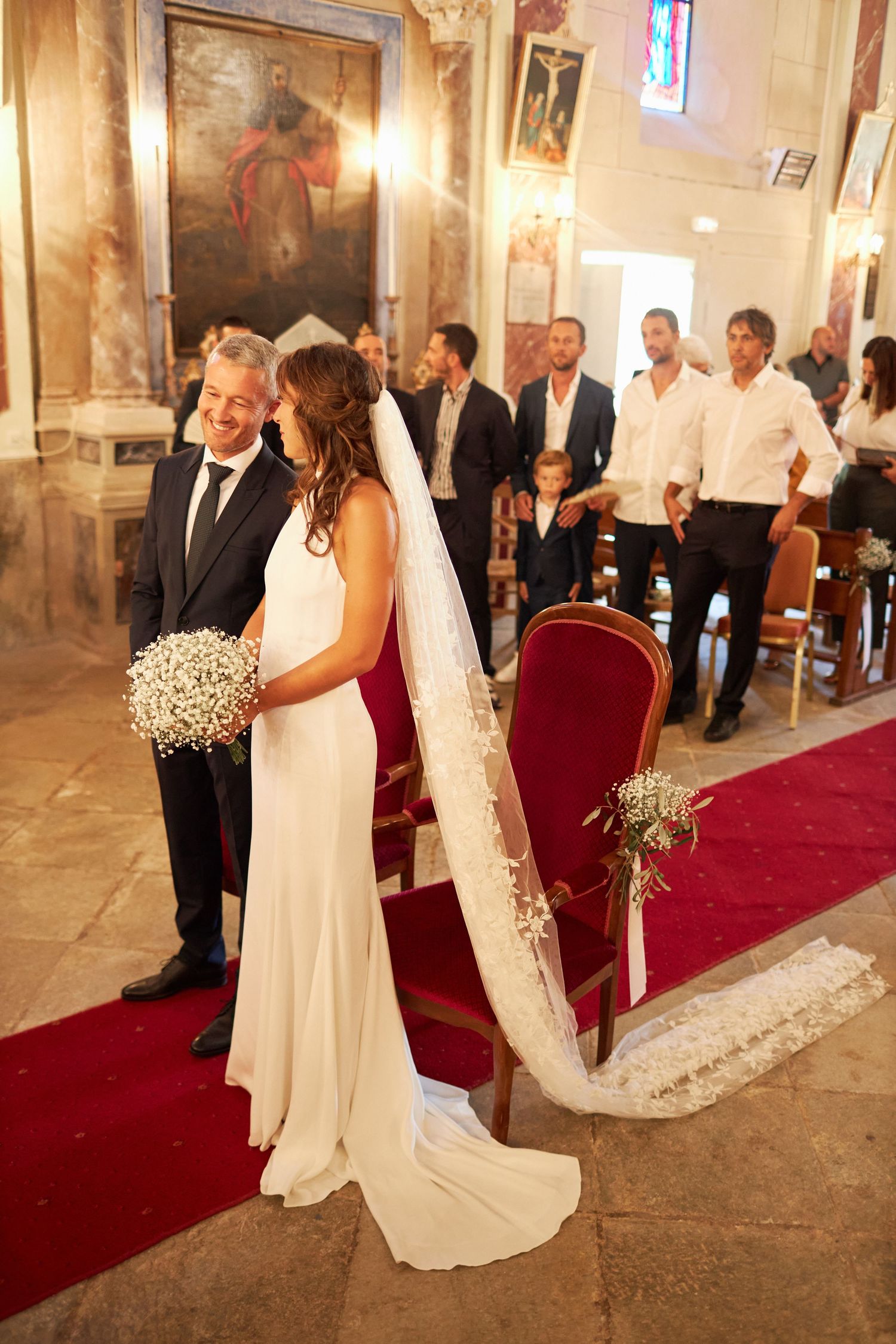 Bride in white gown with veil and groom in suit stand at church altar during wedding ceremony.
