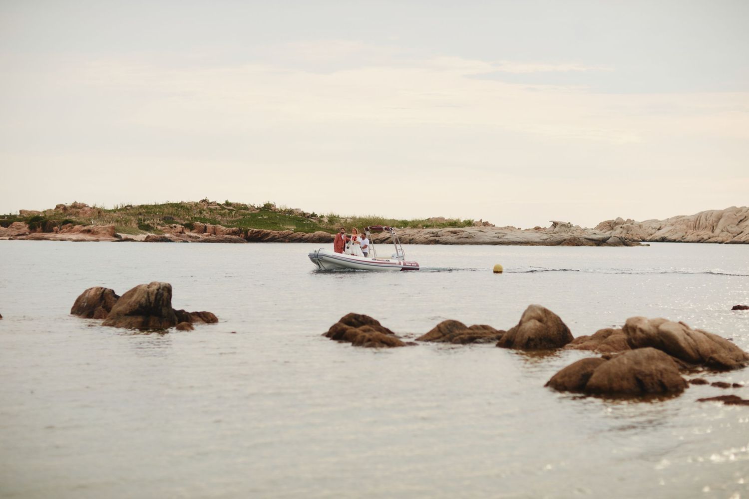Small motorboat navigating calm coastal waters surrounded by rocky shoreline on a cloudy day.