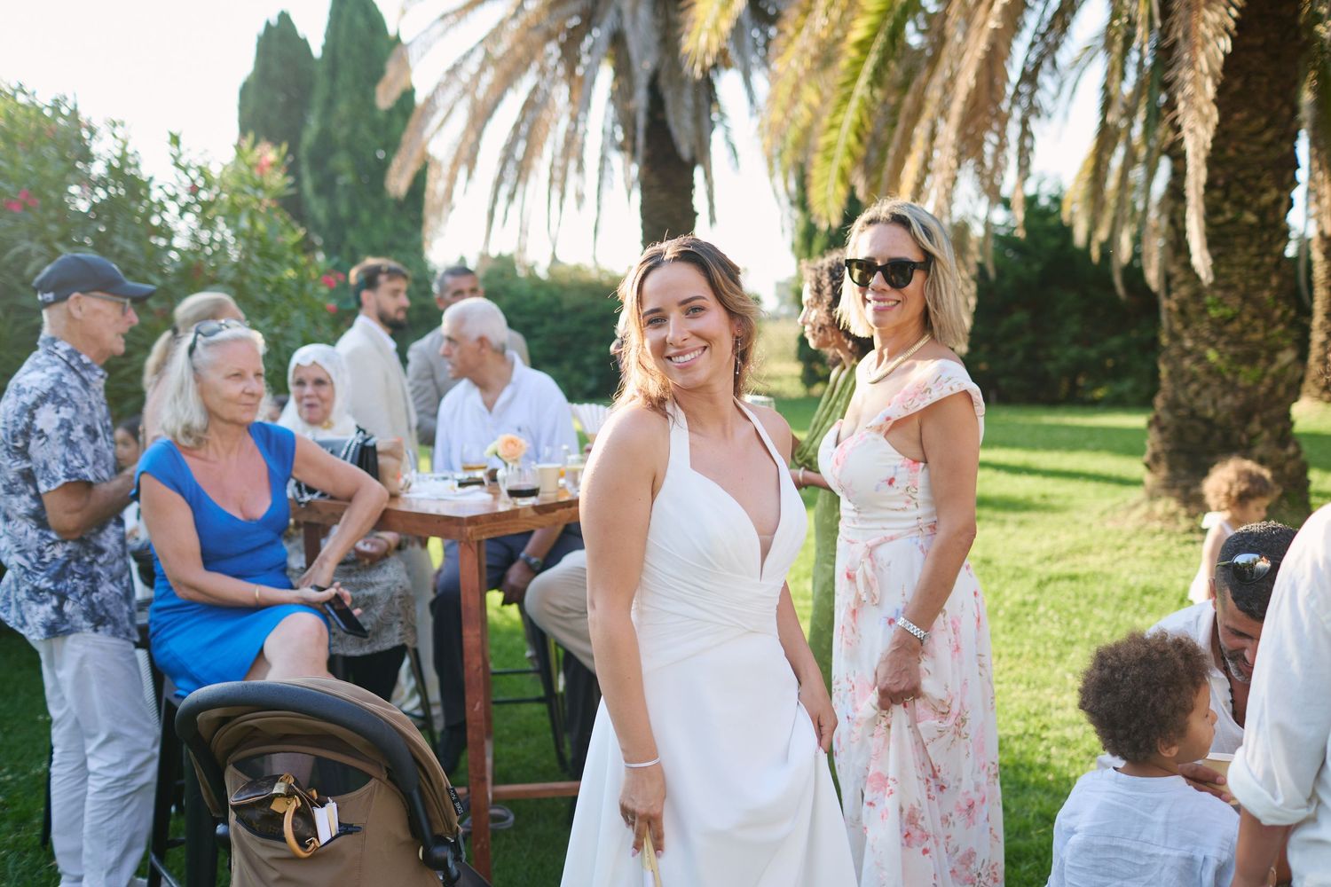 Radiant bride in white halter dress mingles with guests during outdoor garden wedding cocktail hour.
