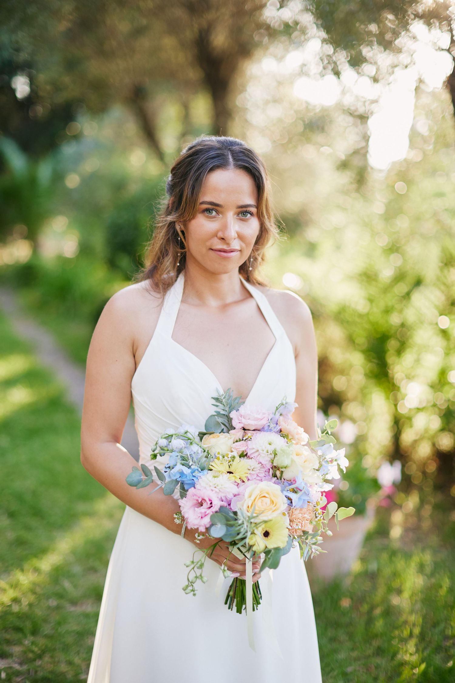 Bride in white halter dress holds colorful pastel bouquet outdoors.