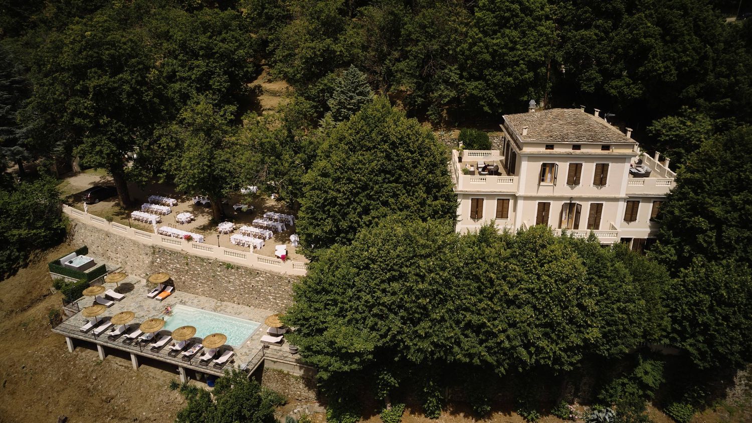 Aerial view of an elegant French countryside villa surrounded by lush trees with a pool and terrace.