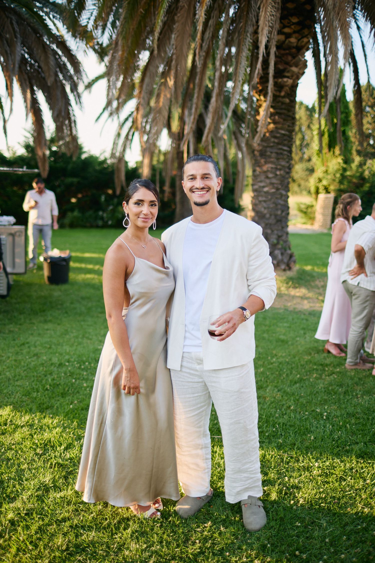 Smiling couple in neutral tones standing on green lawn at outdoor wedding.