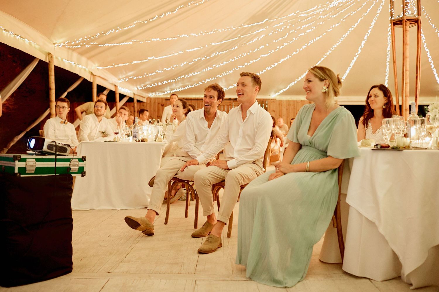 Wedding guests laugh and smile while seated at a beautifully decorated beach reception tent.