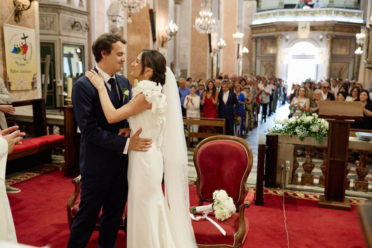 Bride and groom share first dance in elegant church ceremony with guests watching in background.