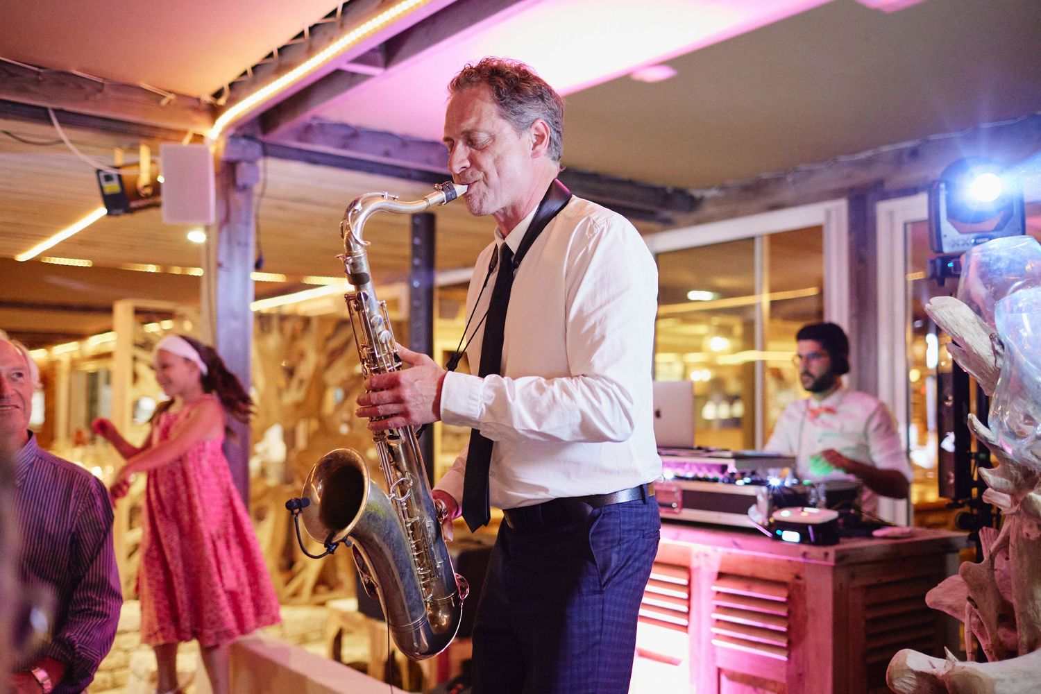 Saxophonist performing live music in white shirt and black tie at a vibrant wedding reception.