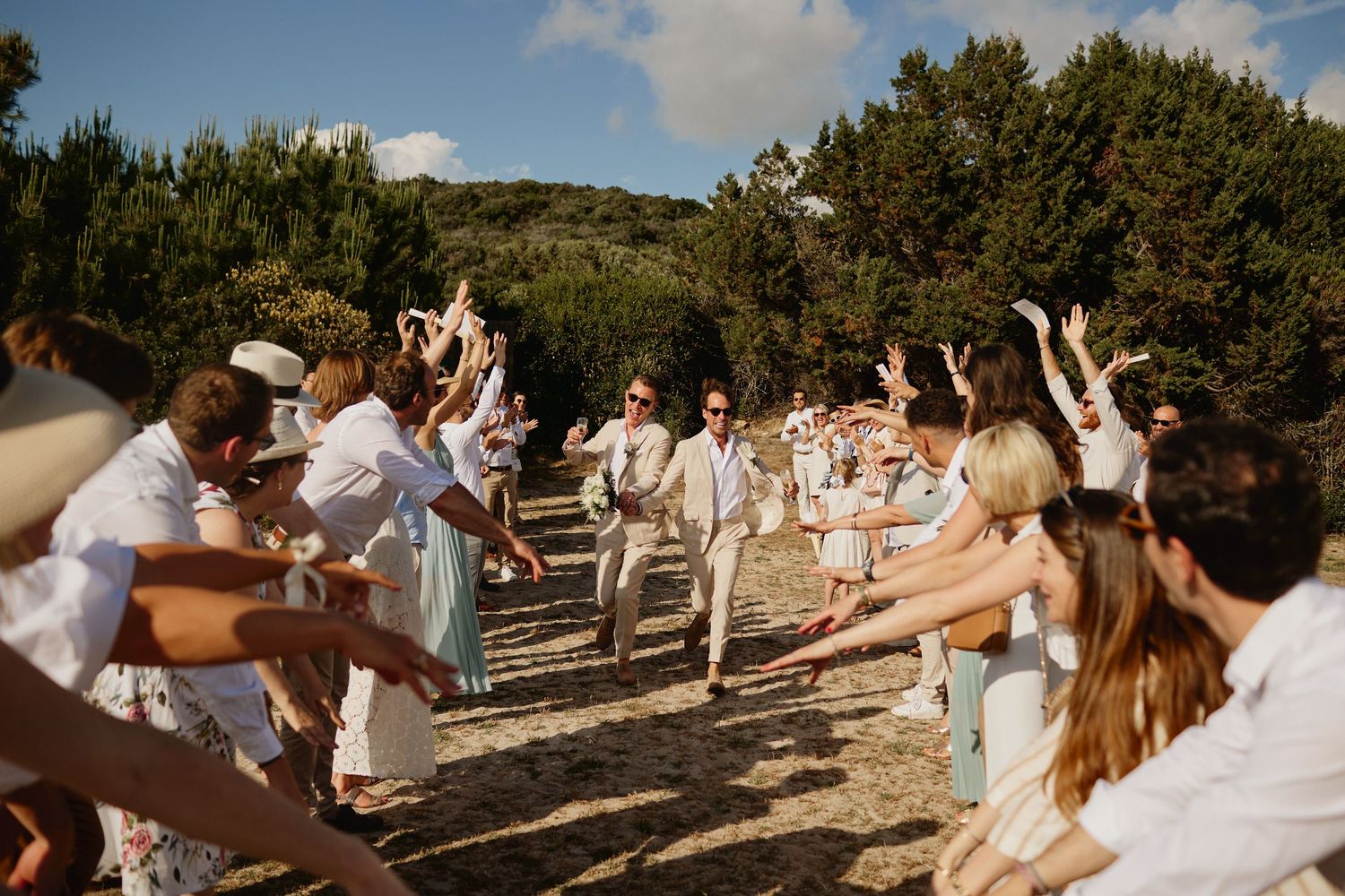 Wedding guests celebrate newlyweds with outstretched arms during joyful outdoor ceremony exit.