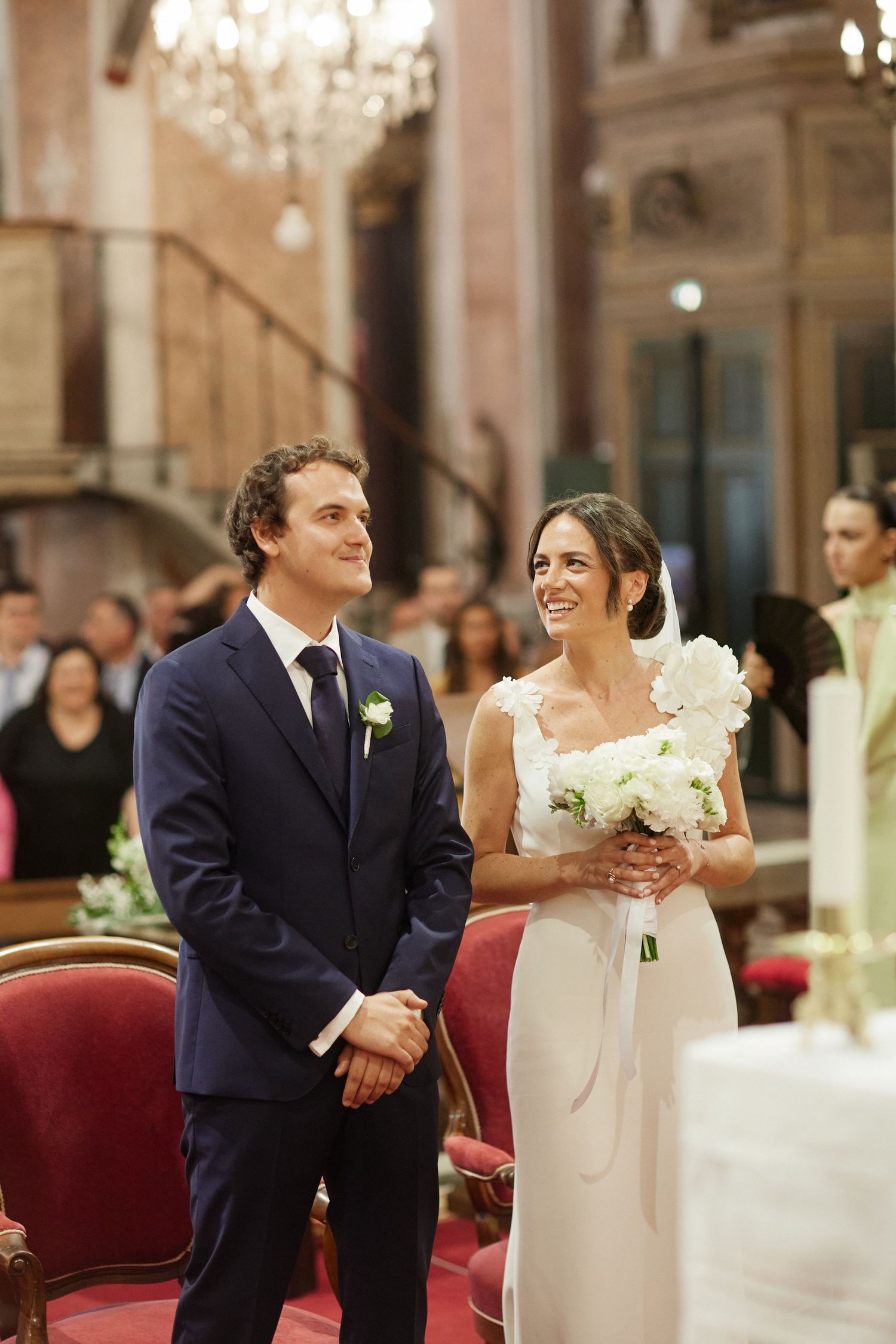 Smiling bride and groom standing at church altar during wedding ceremony with guests seated.