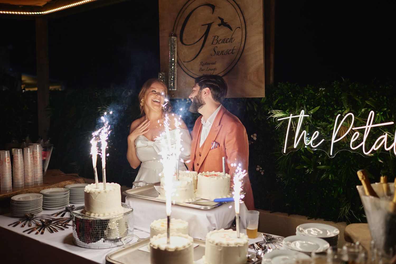 Bride and groom cutting wedding cake with sparklers at The Petals venue dessert table.
