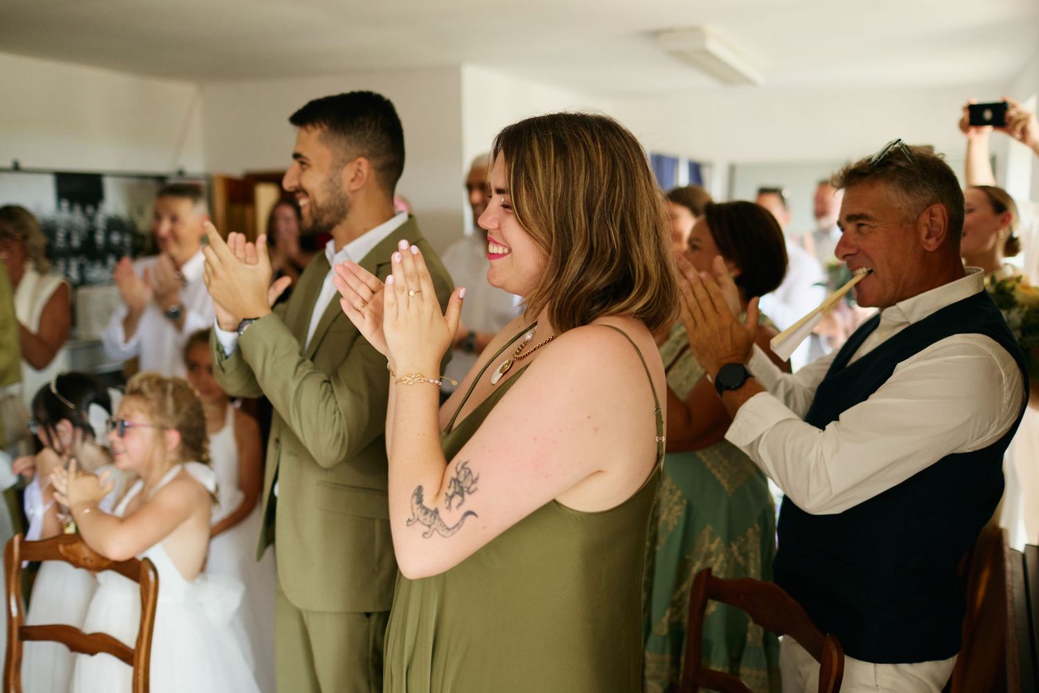 Wedding guests in elegant attire clapping and celebrating during an indoor ceremony.