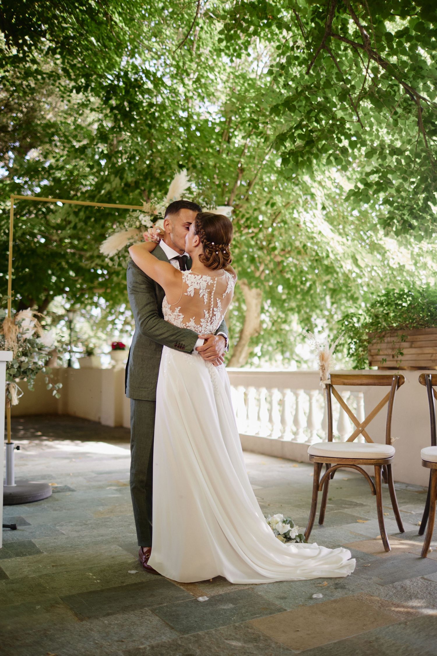 Newlyweds embracing in first dance under lush green tree canopy at outdoor wedding ceremony venue.