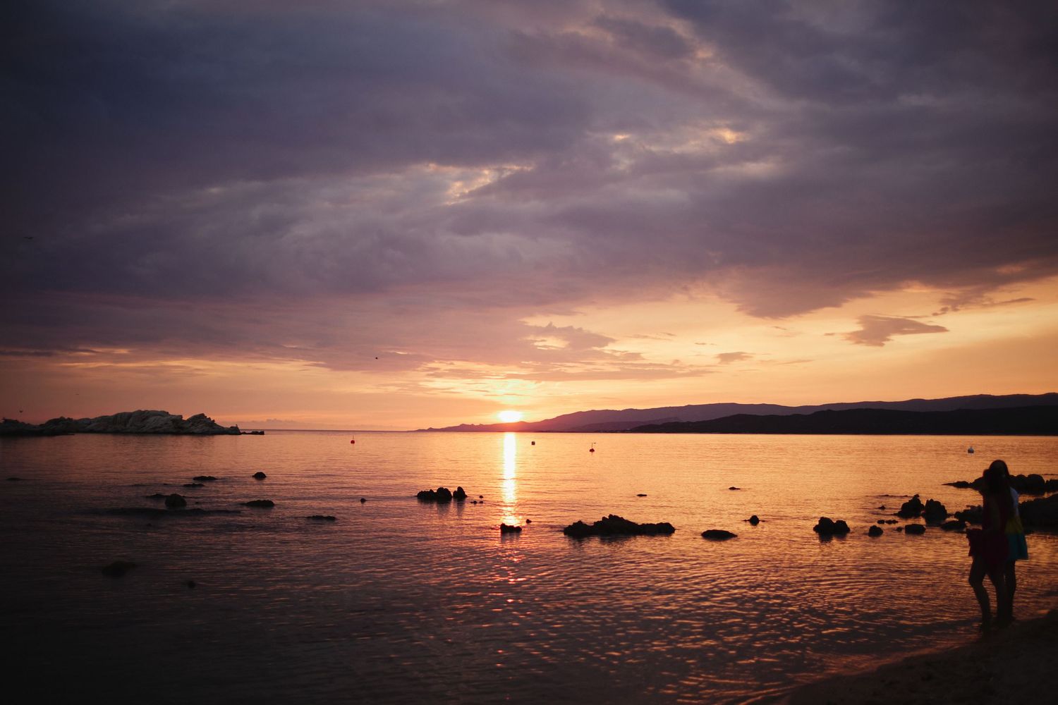 Silhouette of a person standing on a beach shore during a dramatic purple and orange sunset.