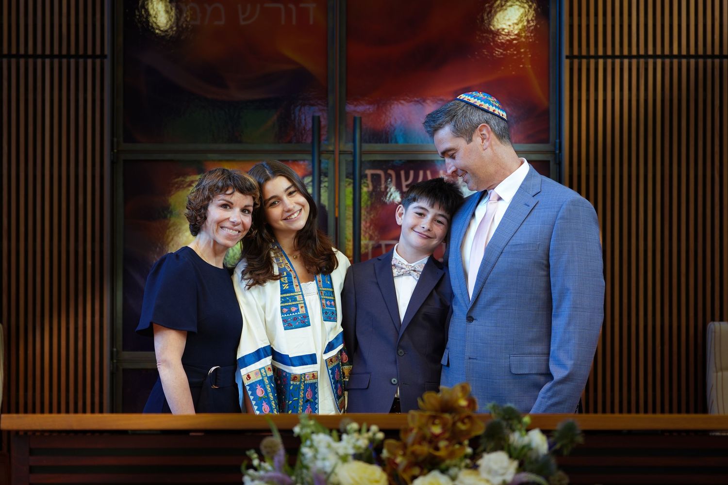 Family posing together at a Bar Mitzvah ceremony in a synagogue, wearing traditional Jewish attire including a tallit.