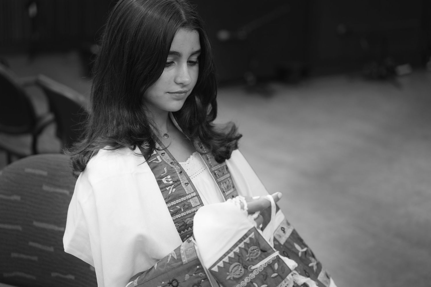 Young woman in traditional embroidered attire reading a book, captured in black and white photography.