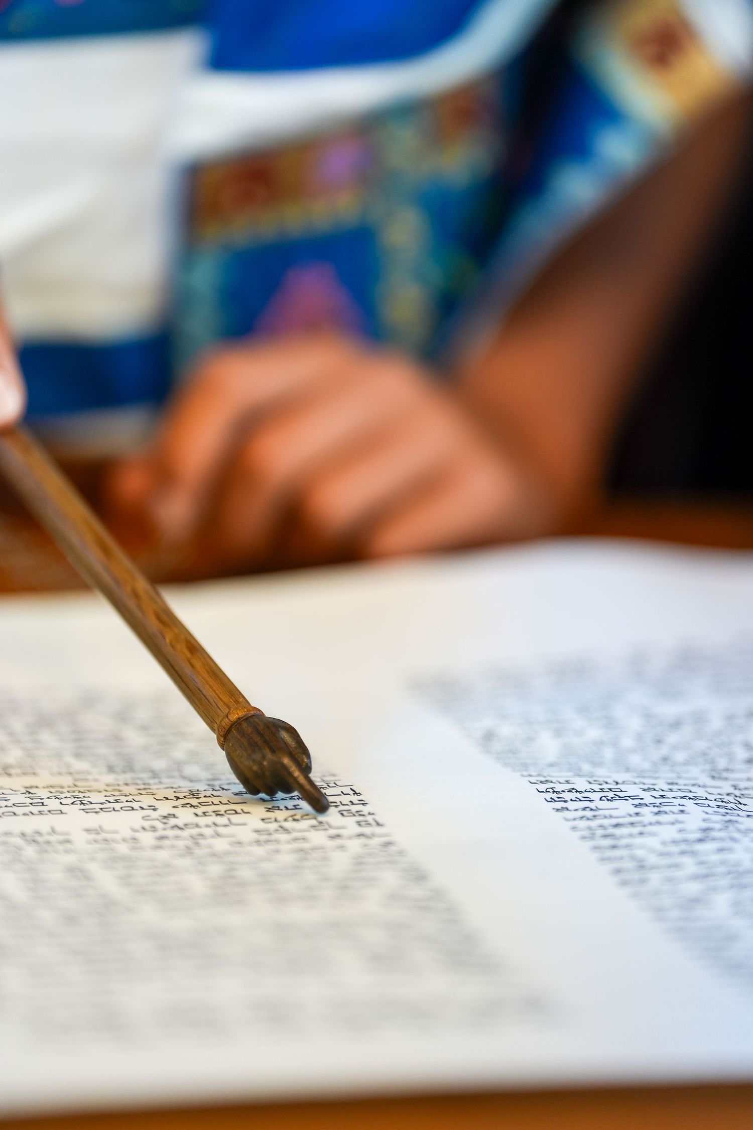 A yad pointer resting on an open Torah scroll during a Jewish religious reading ceremony.