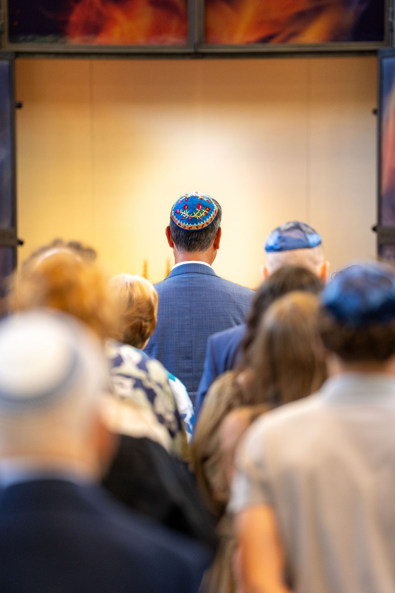 Jewish congregation wearing kippot gathered in prayer at a synagogue during a religious ceremony.