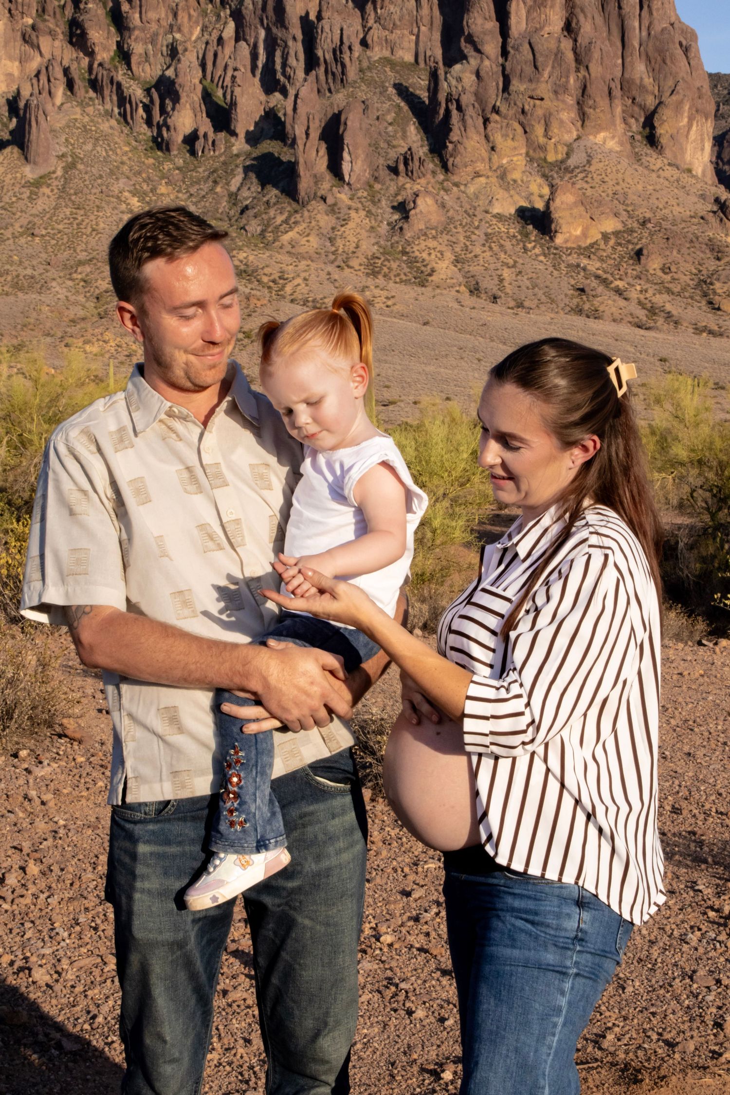 Smiling couple with man holding toddler girl in desert mountain setting.