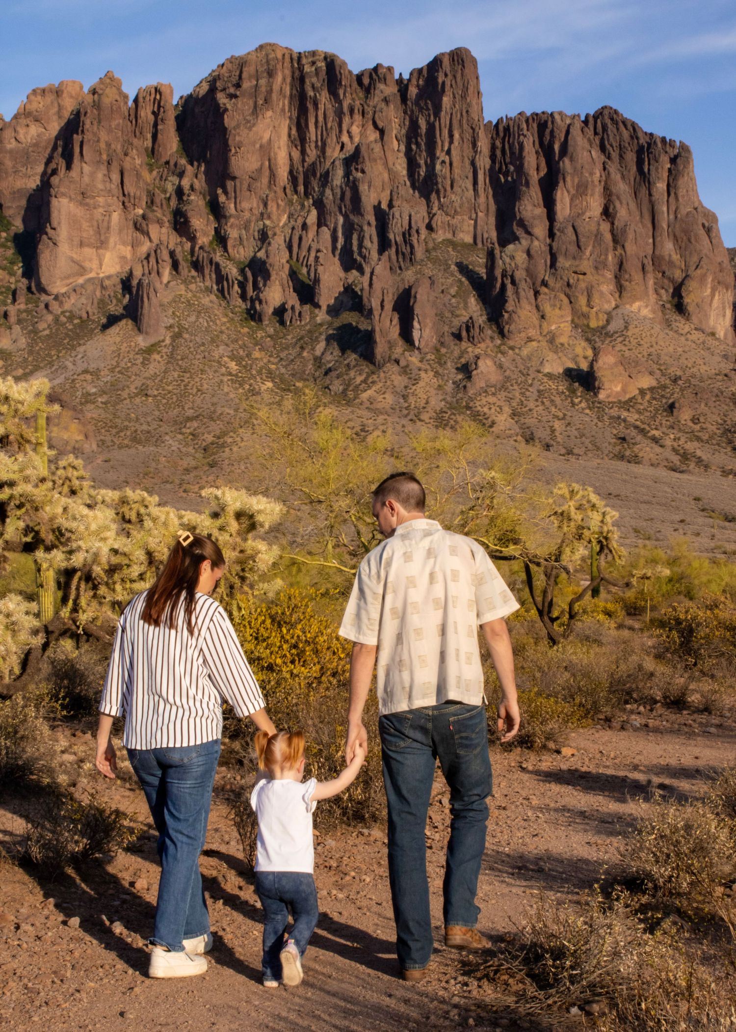 Family of three walking toward rugged mountain on scenic desert trail at sunset.