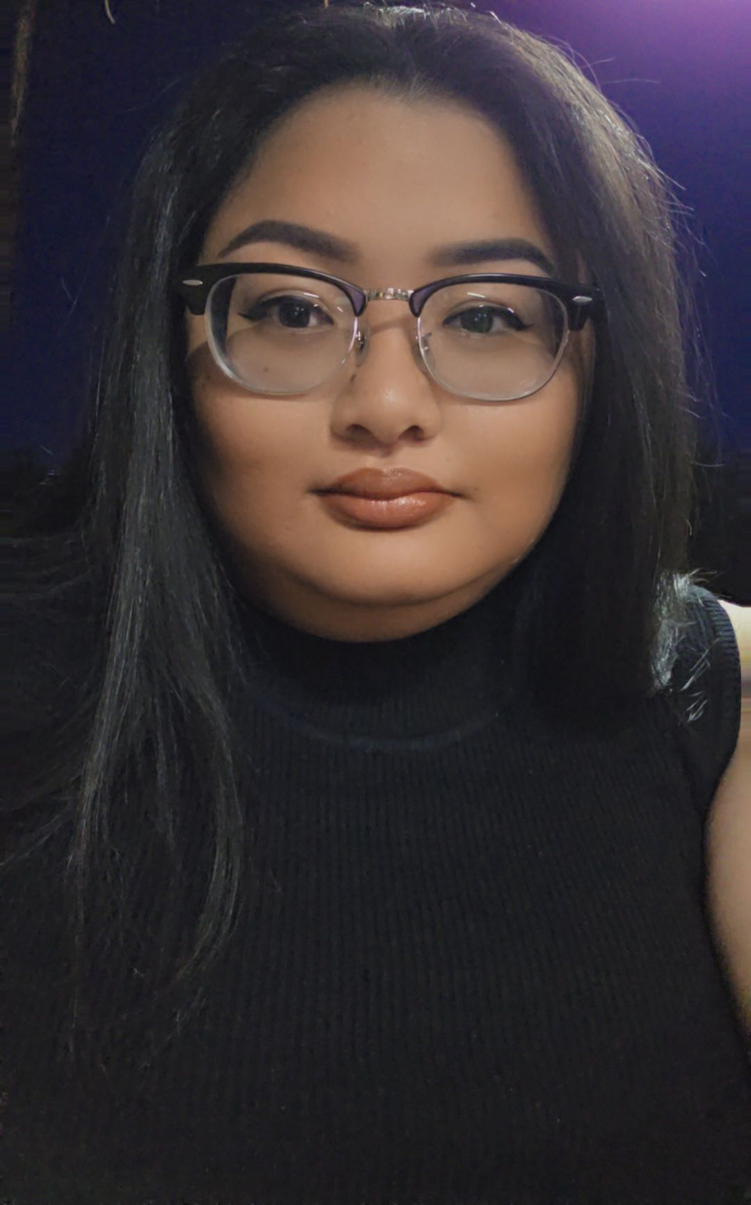 Young woman with long dark hair wearing glasses and a black turtleneck posing for a close-up portrait.