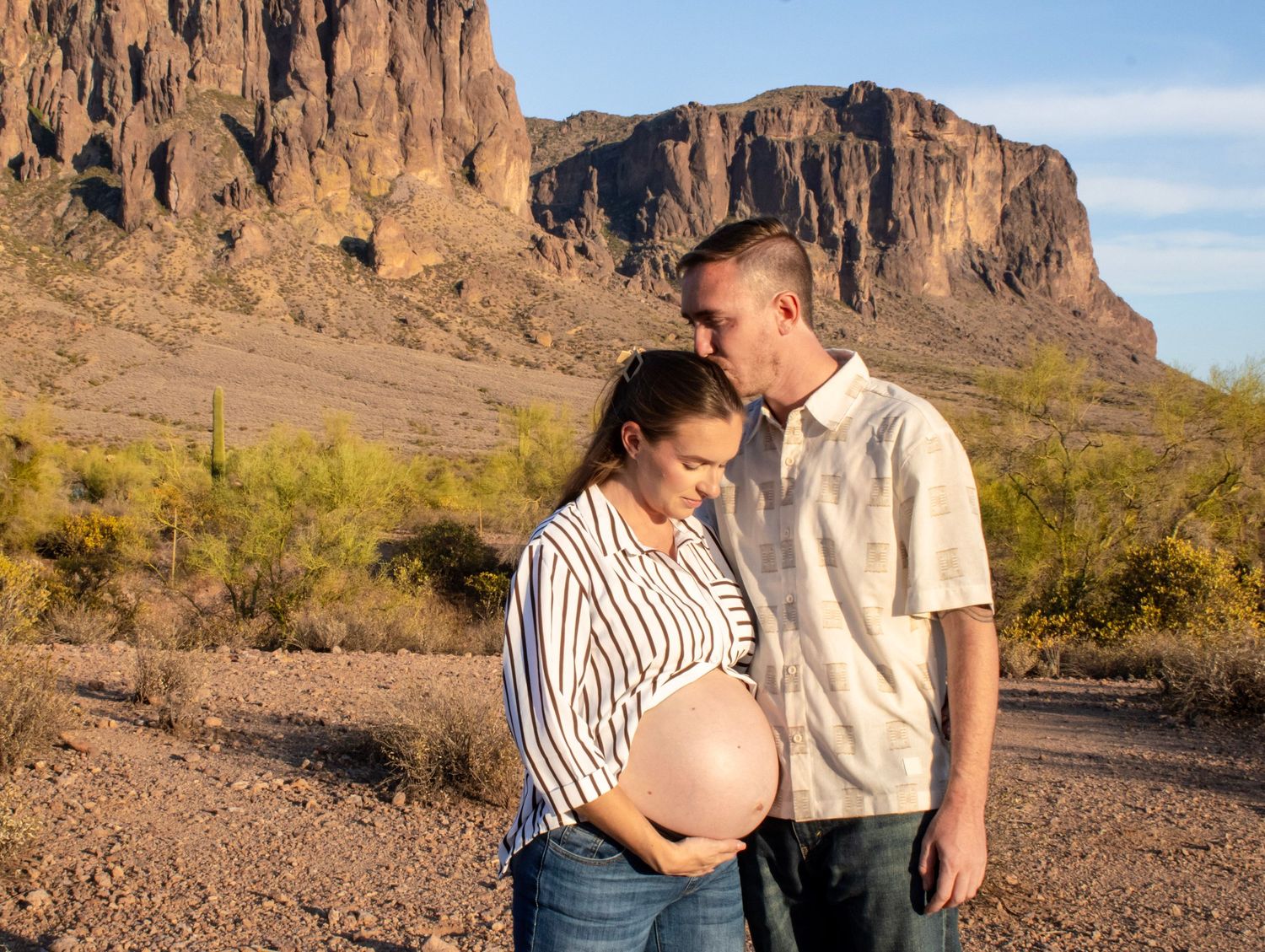 Pregnant couple sharing a tender moment in the Arizona desert with Superstition Mountains in the background.