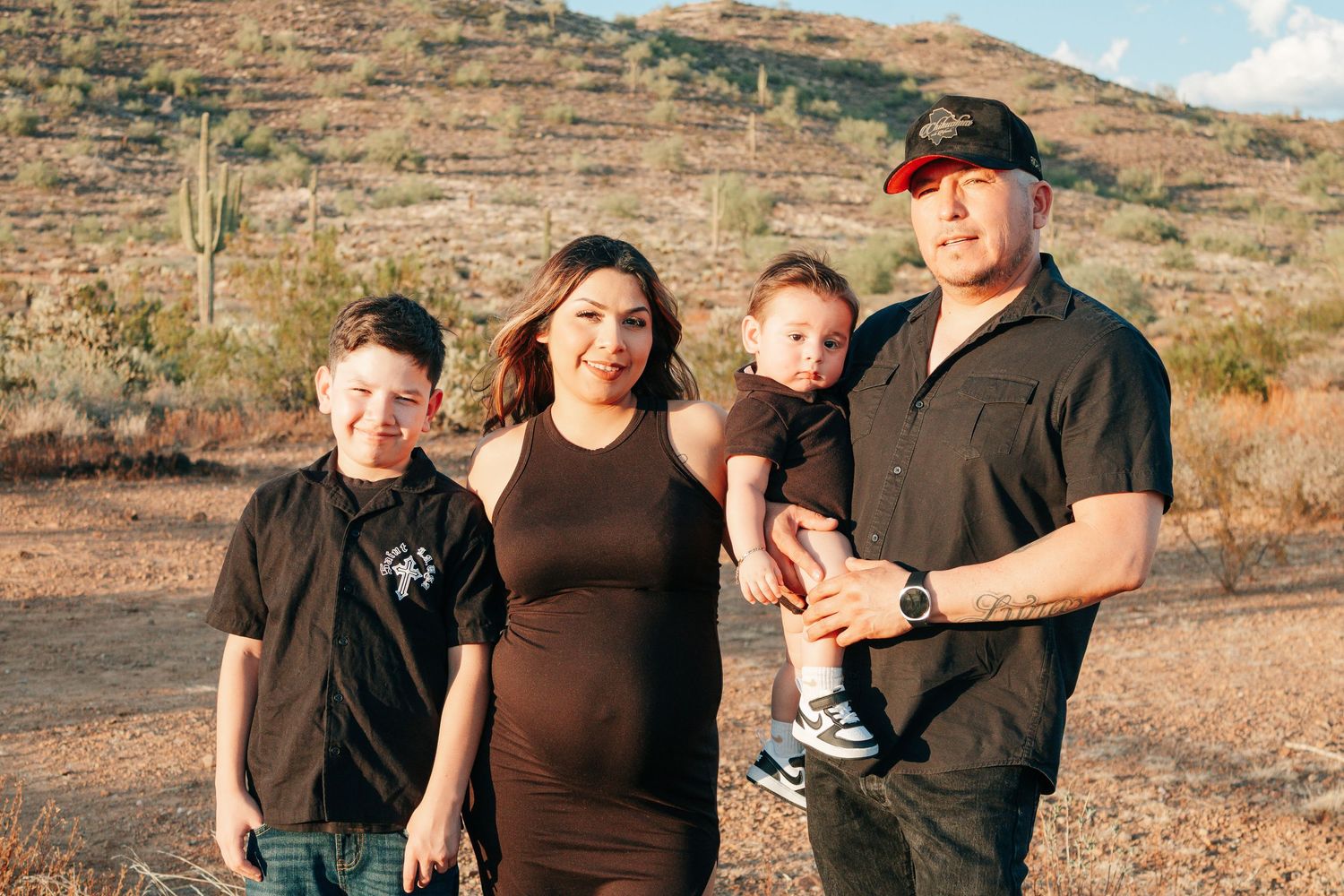 Family of four poses outdoors in desert landscape with saguaro cacti and rocky hills in background.