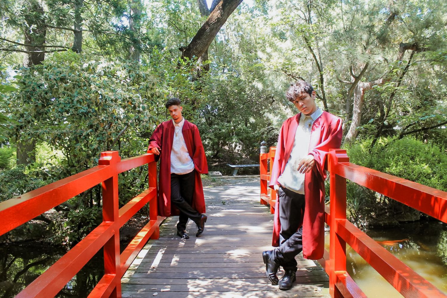 Two men in red traditional robes posing on red Japanese garden bridge.