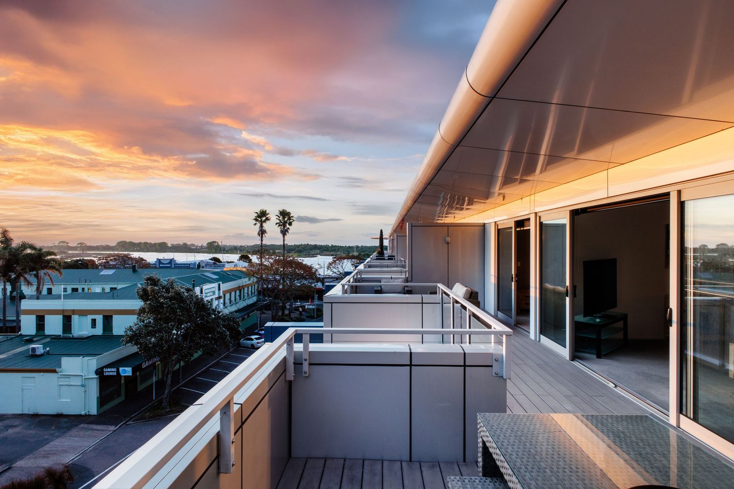 Luxury balcony overlooking coastal town during dramatic orange and pink sunset.