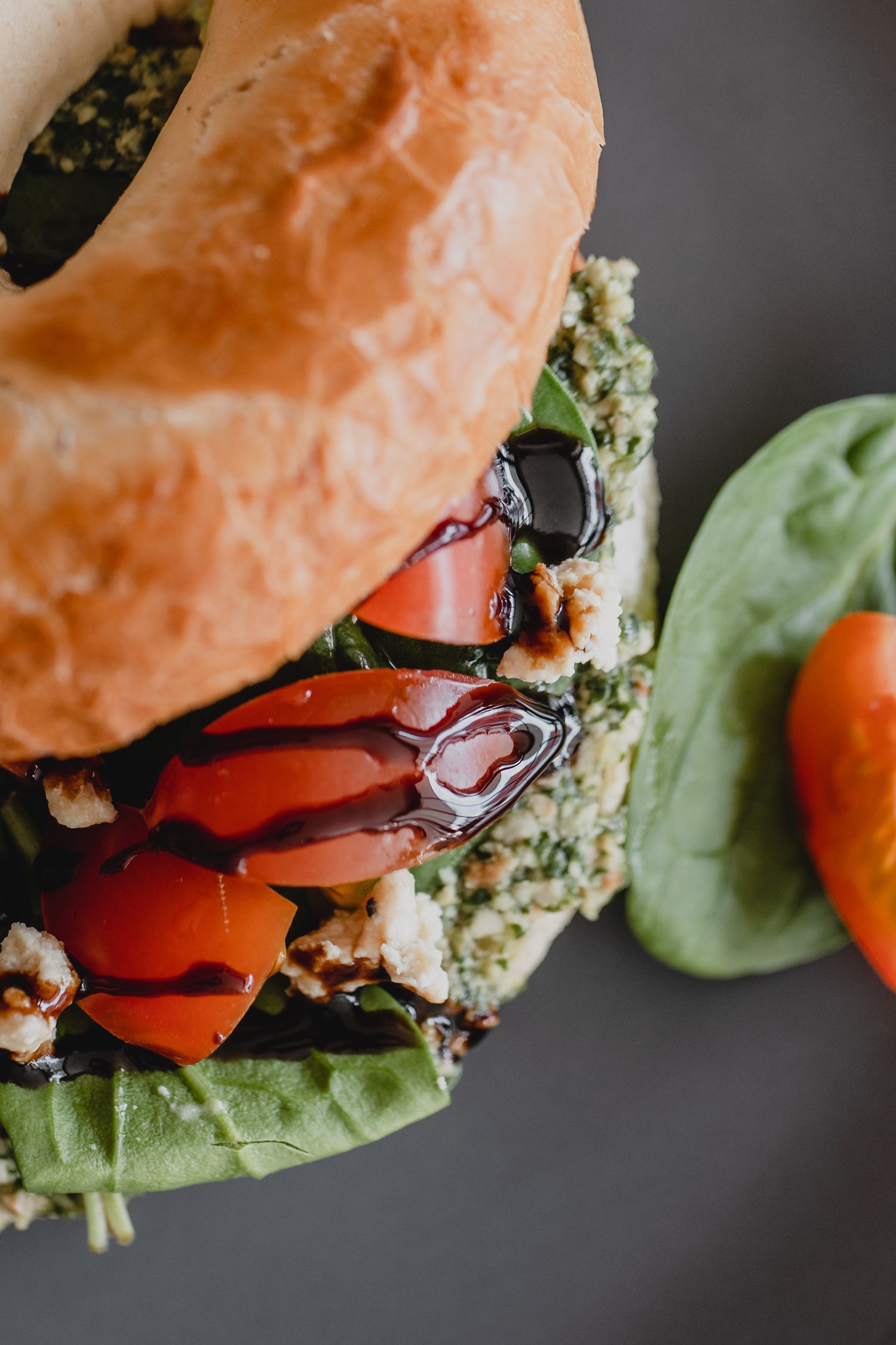 Fresh bagel sandwich loaded with vegetables and spreads on dark background.