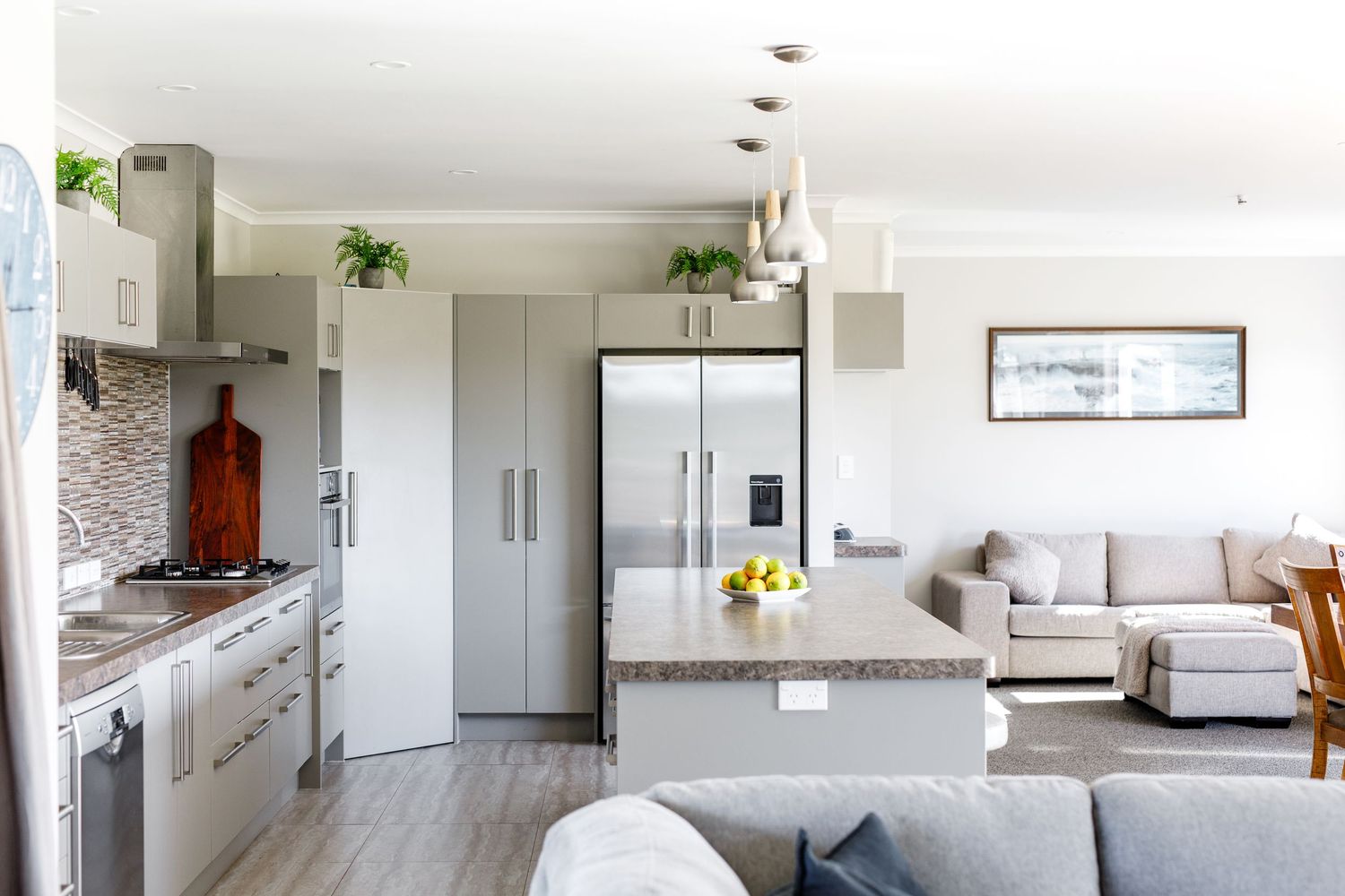 Open concept kitchen and living space with grey sectional sofa and modern appliances.