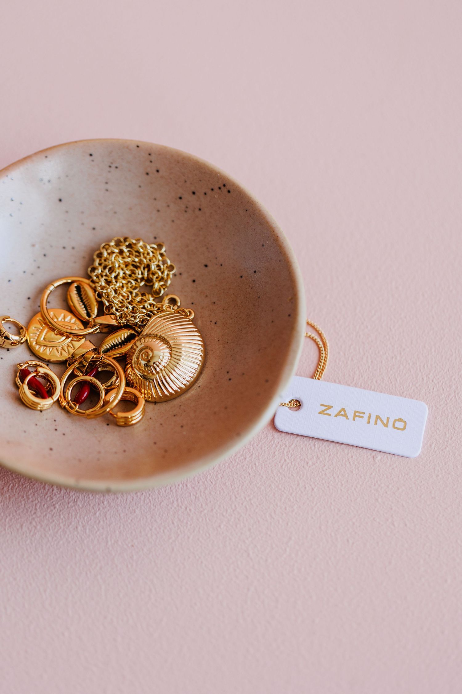 Gold jewelry pieces arranged in a speckled ceramic bowl with Zafino tag.