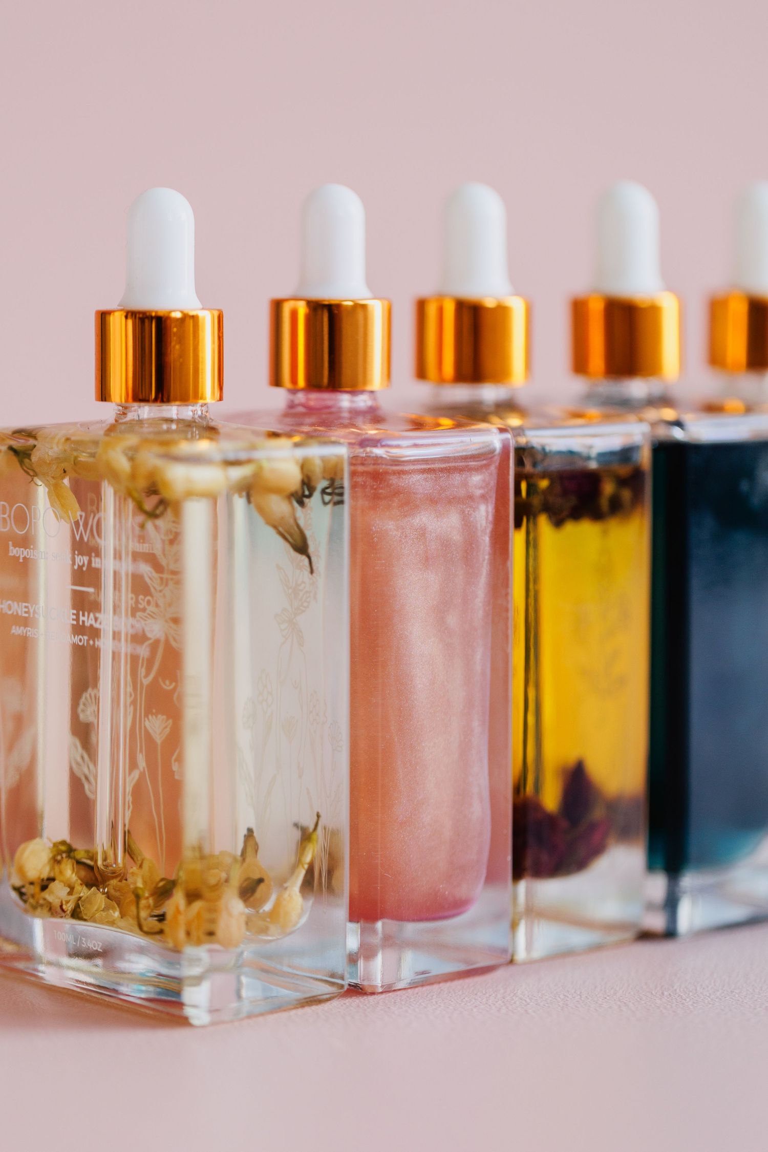 Row of colorful body oil bottles with gold droppers displaying gradient colors from clear to blue.