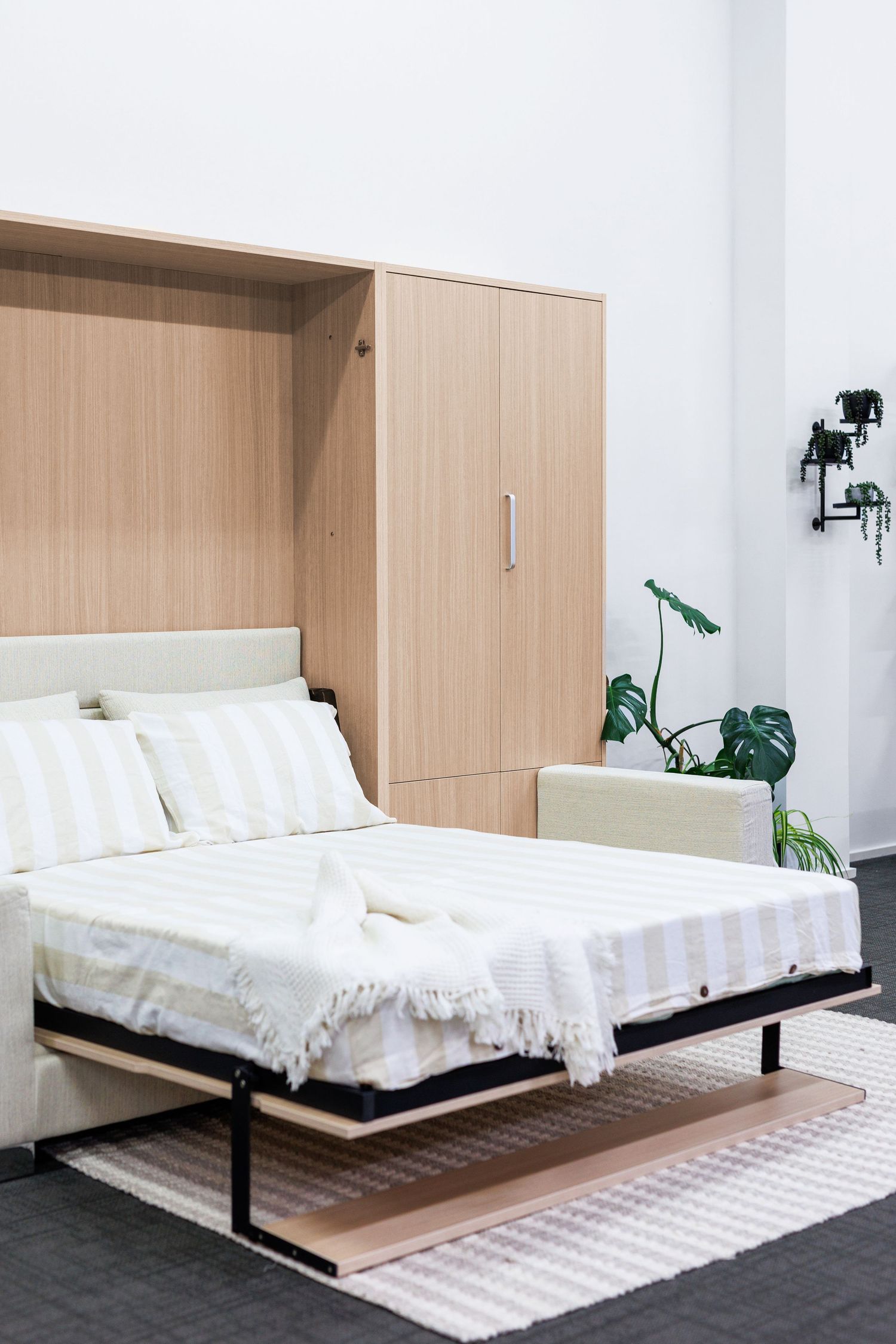 Minimalist murphy bed with white bedding and wooden storage unit in contemporary bedroom.