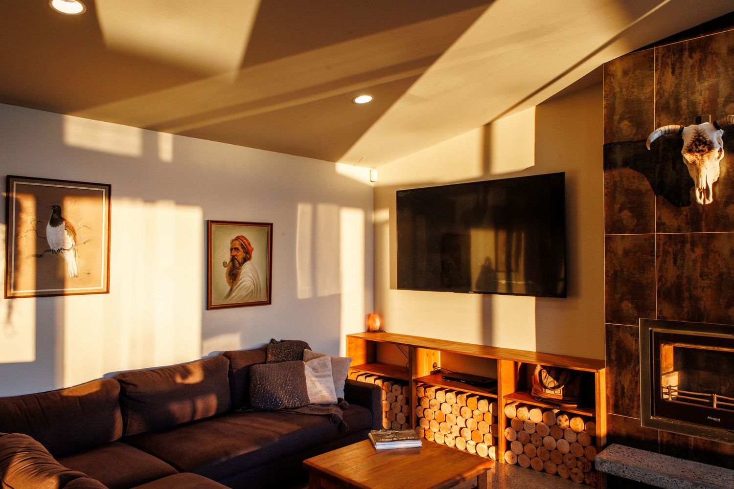 Cozy living room with dark leather couch, mounted TV and warm ambient lighting.