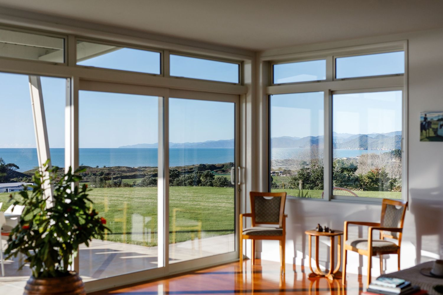 Modern living room with panoramic windows overlooking a coastal landscape and green lawn.