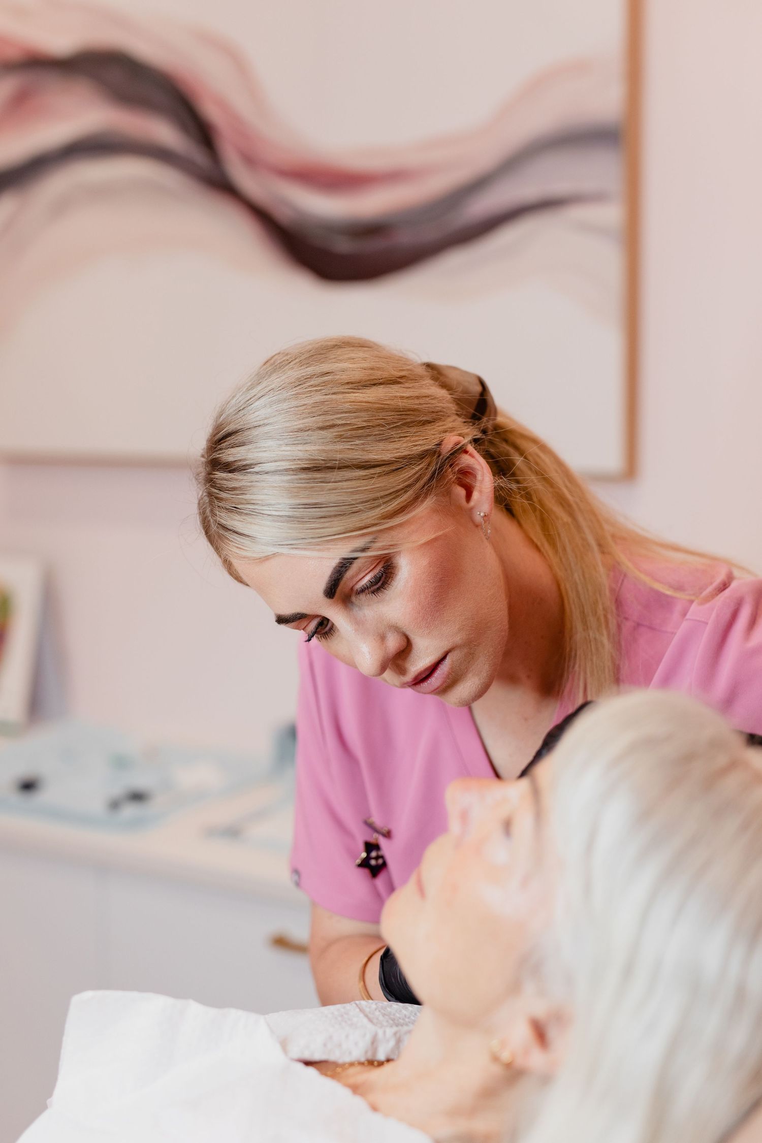 Healthcare provider in pink scrubs performing a facial treatment in a bright medical spa setting.
