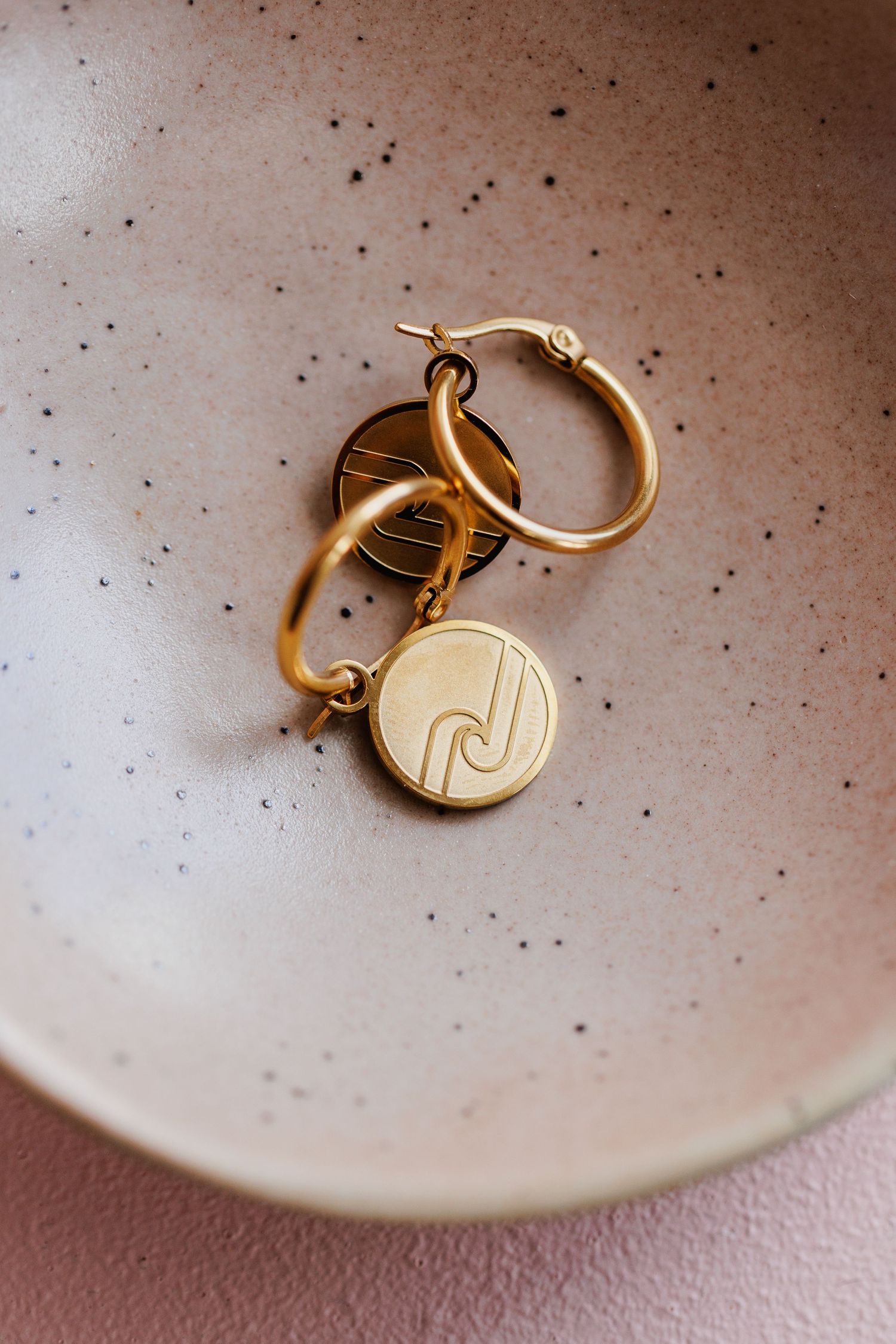 Gold keychain with circular pendant sitting in speckled ceramic bowl.