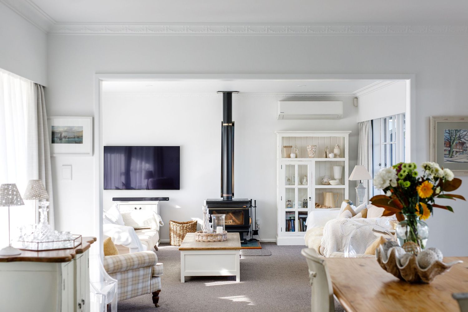 Coastal style living room with wood stove, white armchairs and fresh flowers on wooden table.