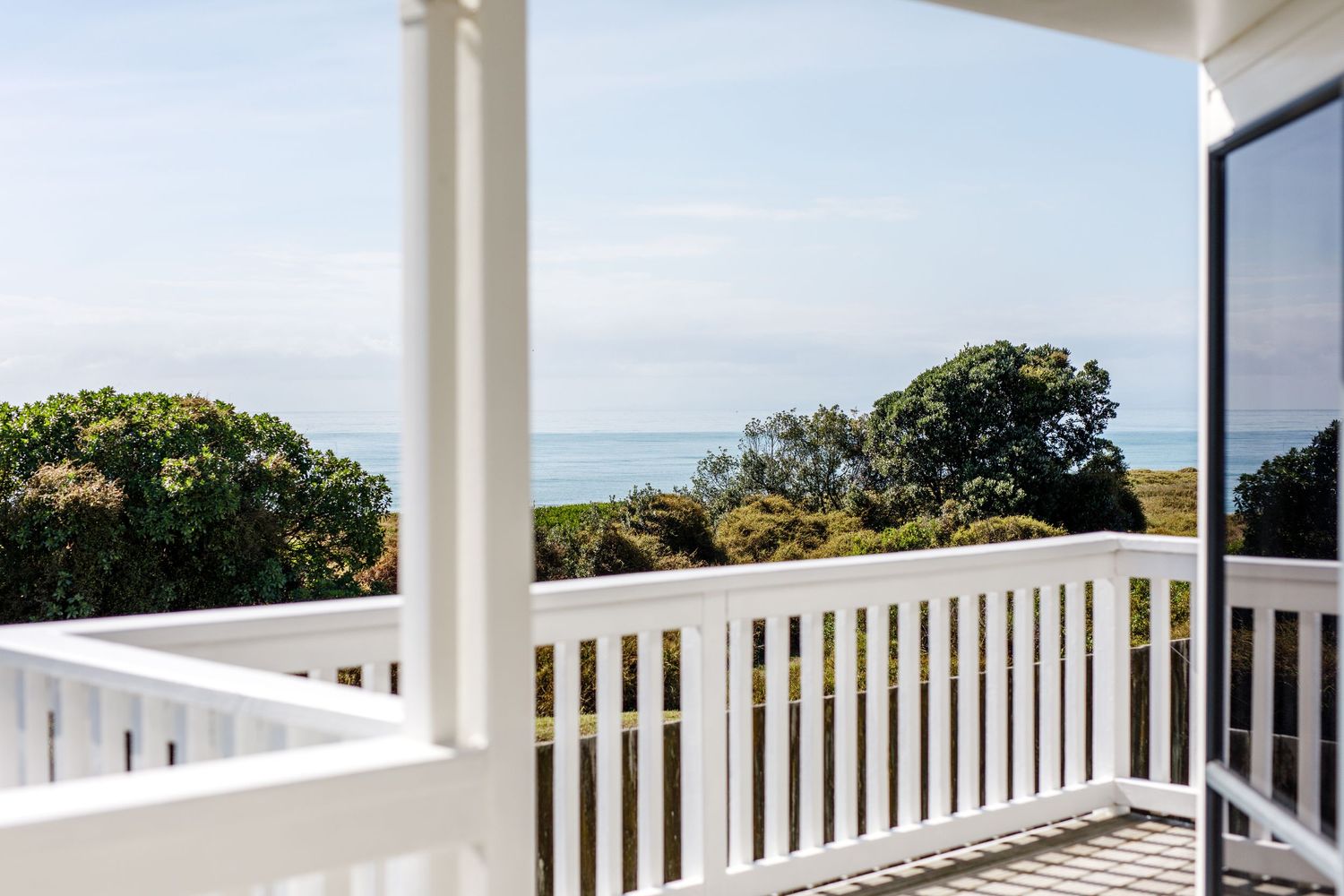 White coastal deck railing with ocean and tree views in background.