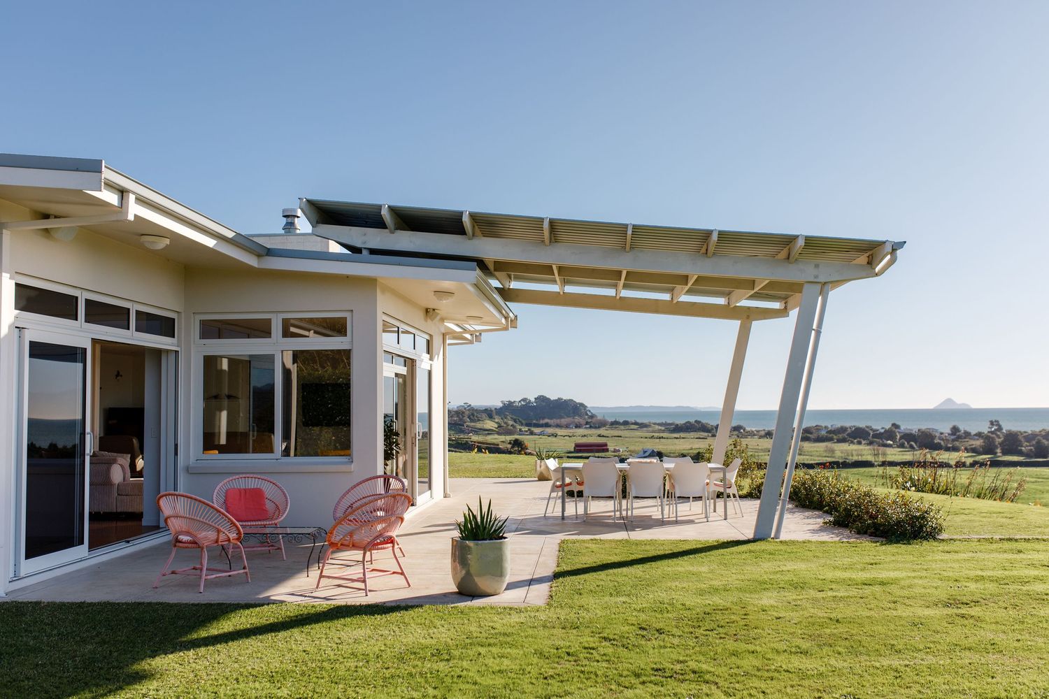 Contemporary house exterior with covered patio and modern pergola overlooking a grassy yard.