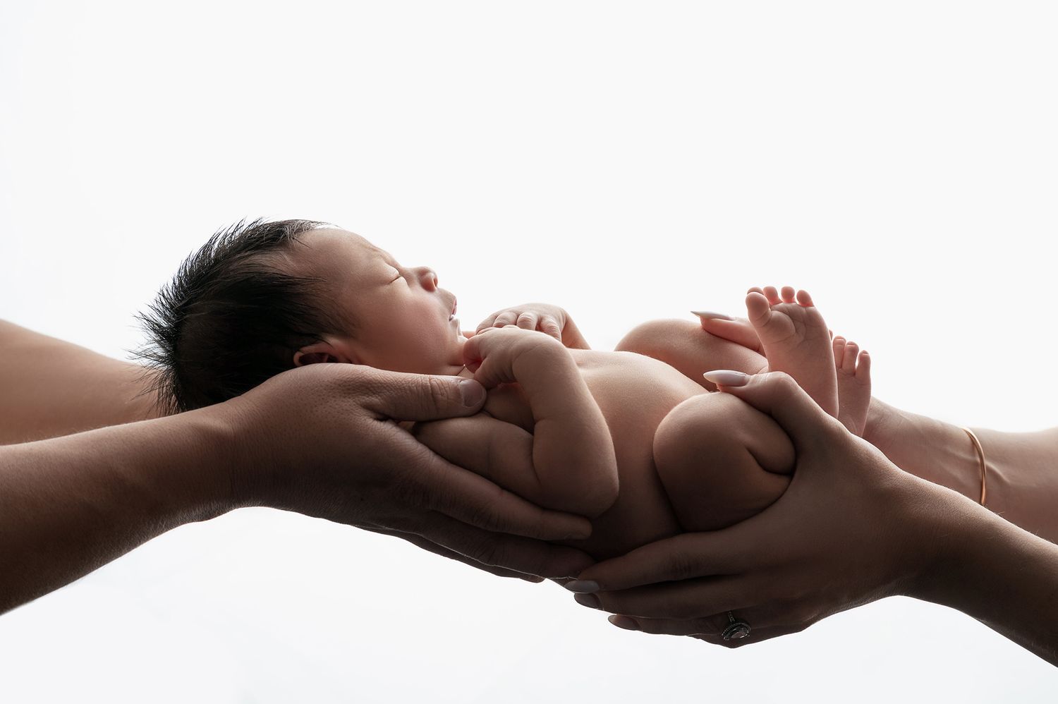 Newborn baby peacefully resting in the gentle, supportive hands of parents against a white background.